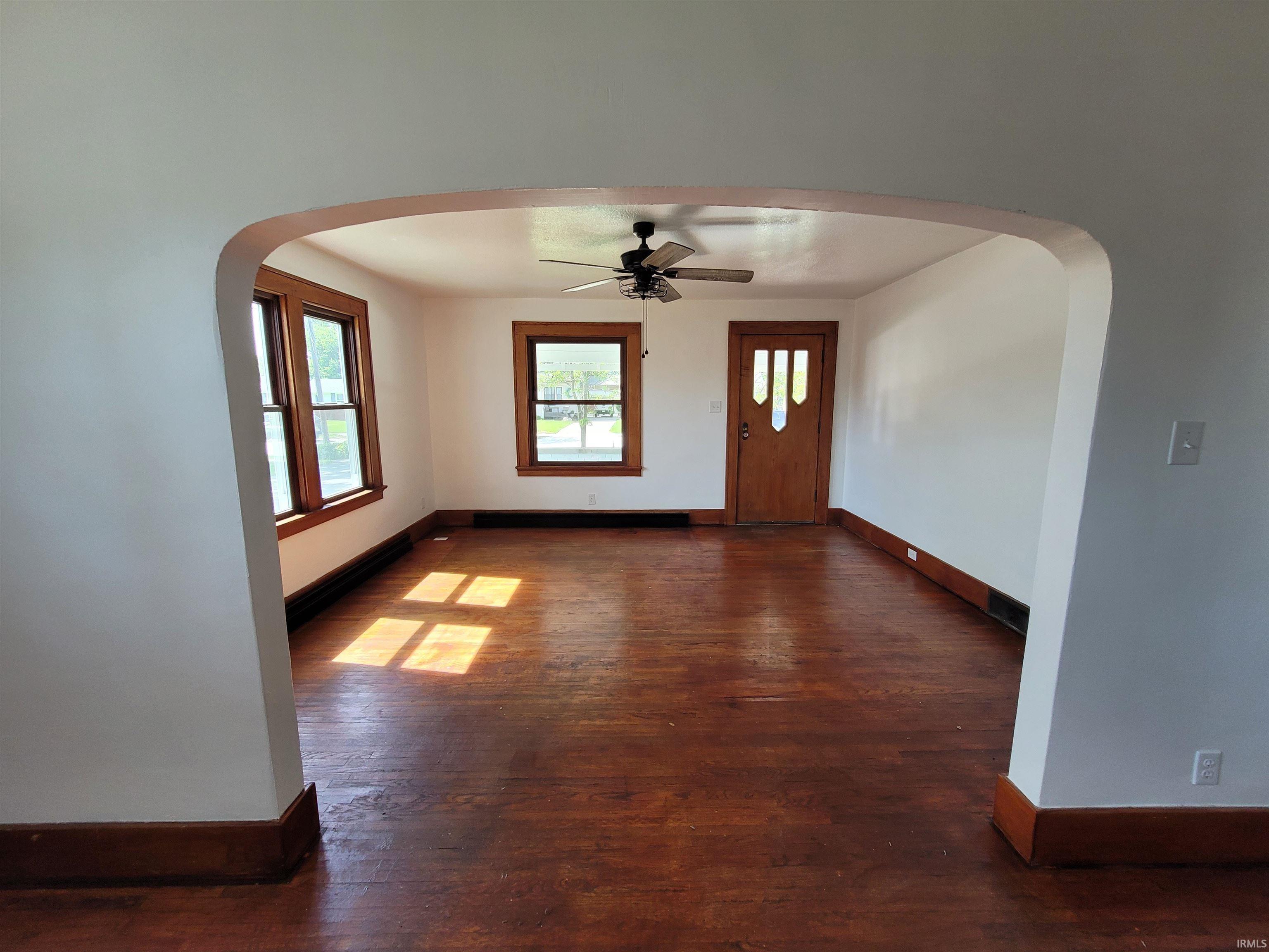 Arched entry to a room featuring warm wood-finish flooring, white walls, and dark wood trim
