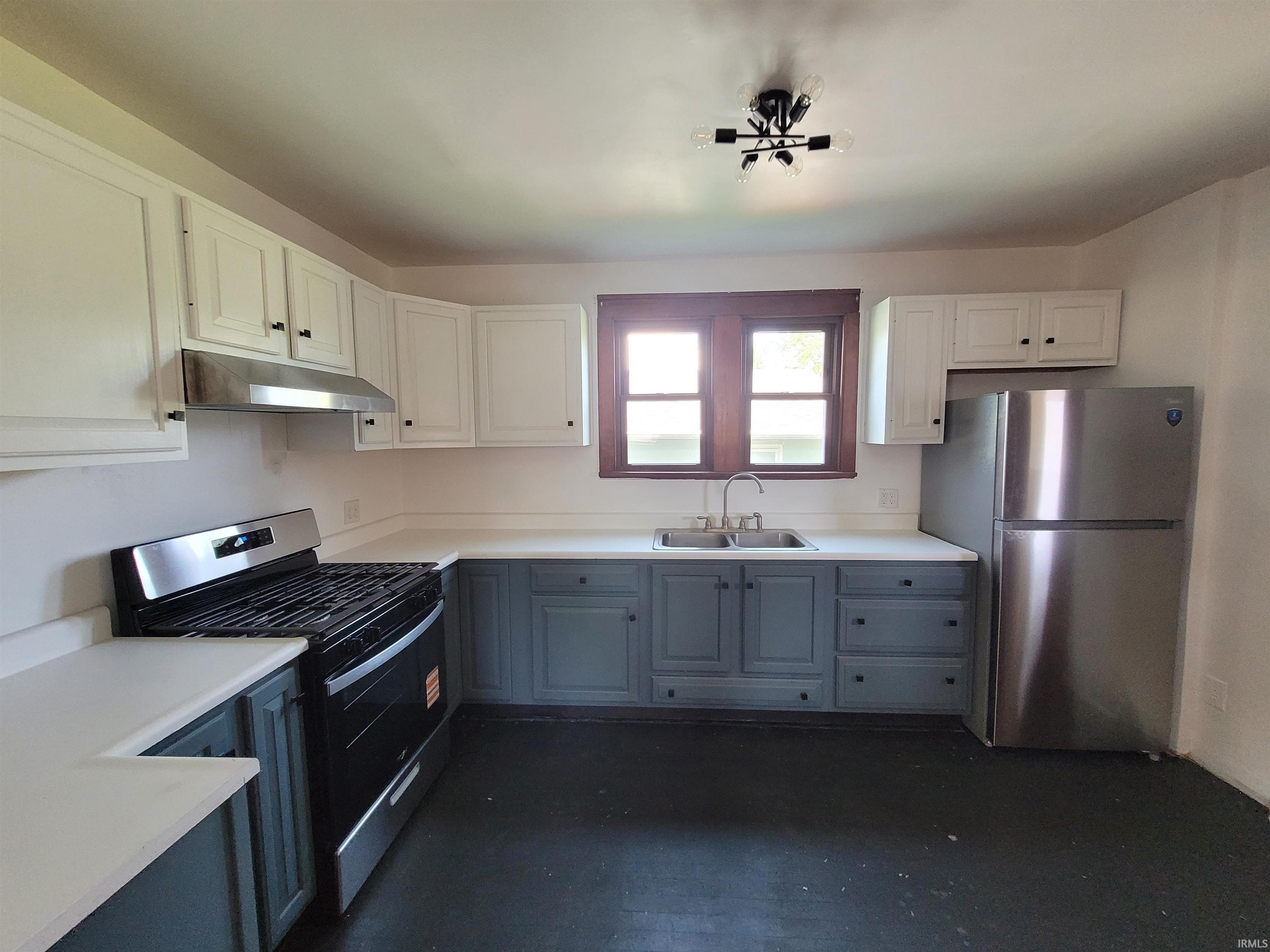 Kitchen featuring two-tone cabinetry with white upper and slate lower cabinets, light-toned countertops, and stainless steel appliances including a range with hood and a refrigerator