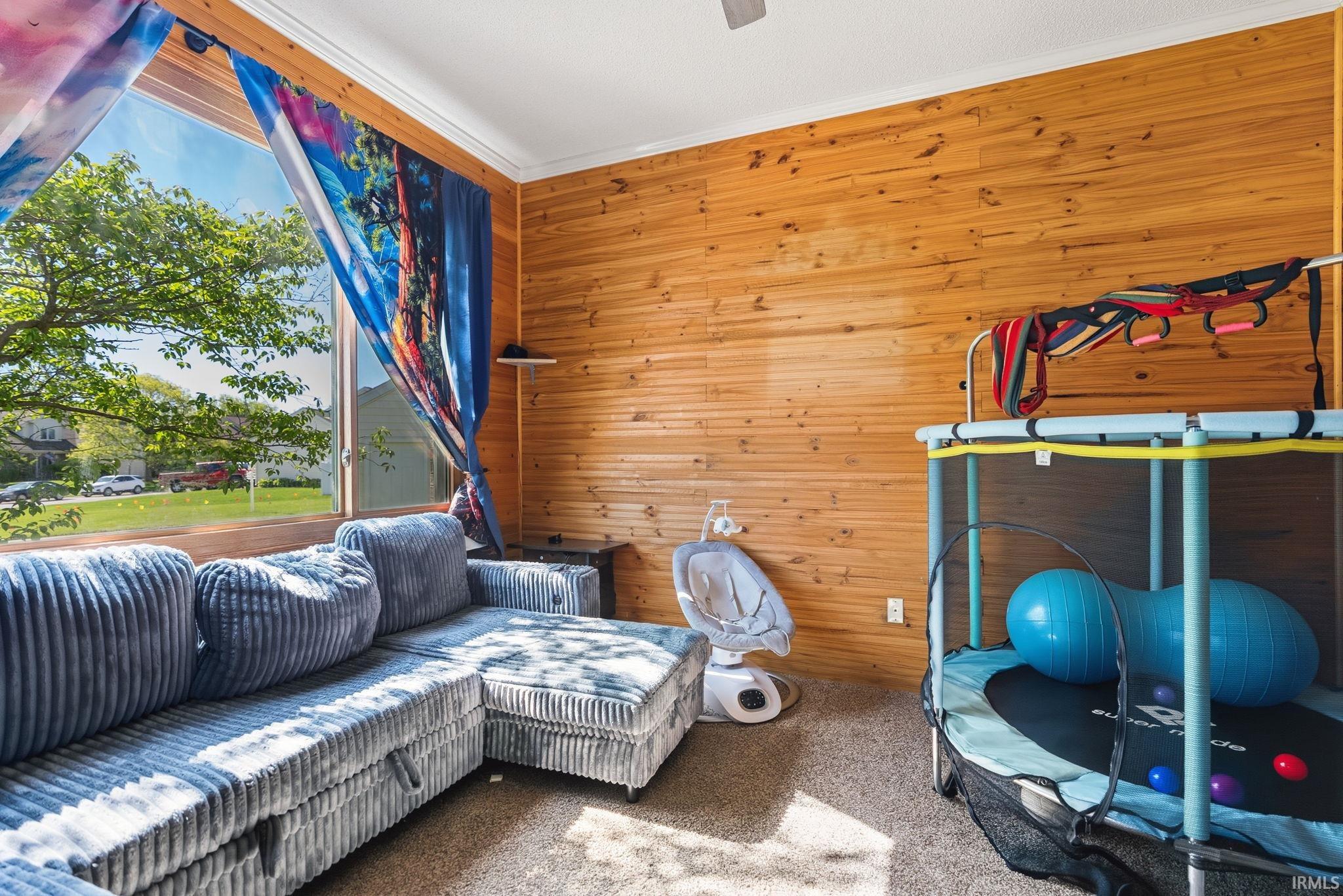 Room featuring wood paneling, a large window, white crown molding, and carpeted flooring