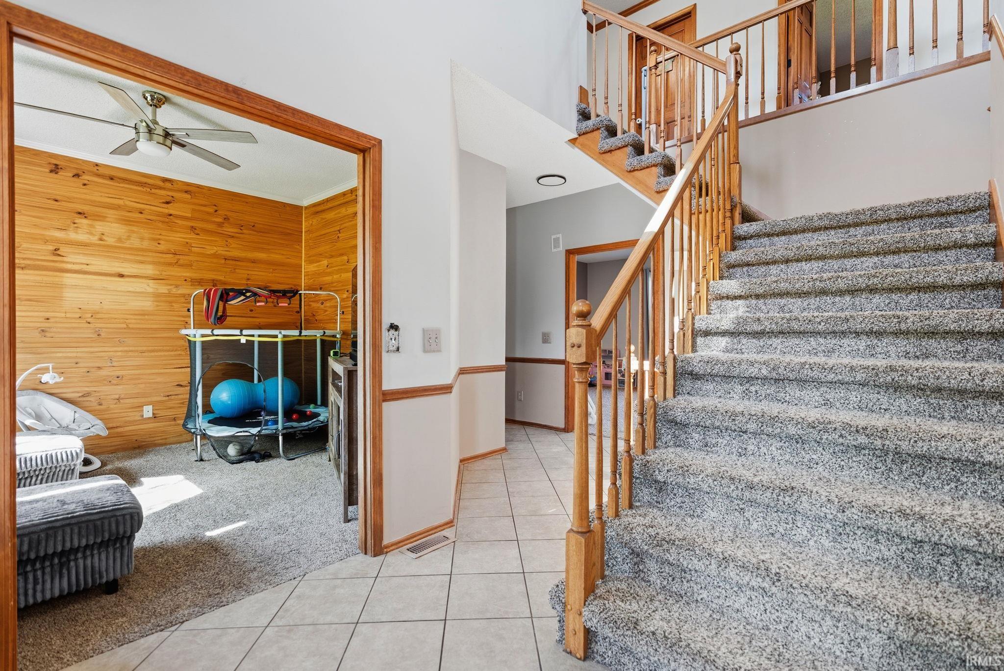 Carpeted staircase with natural wood railing, contrasting with light tile flooring in the entry