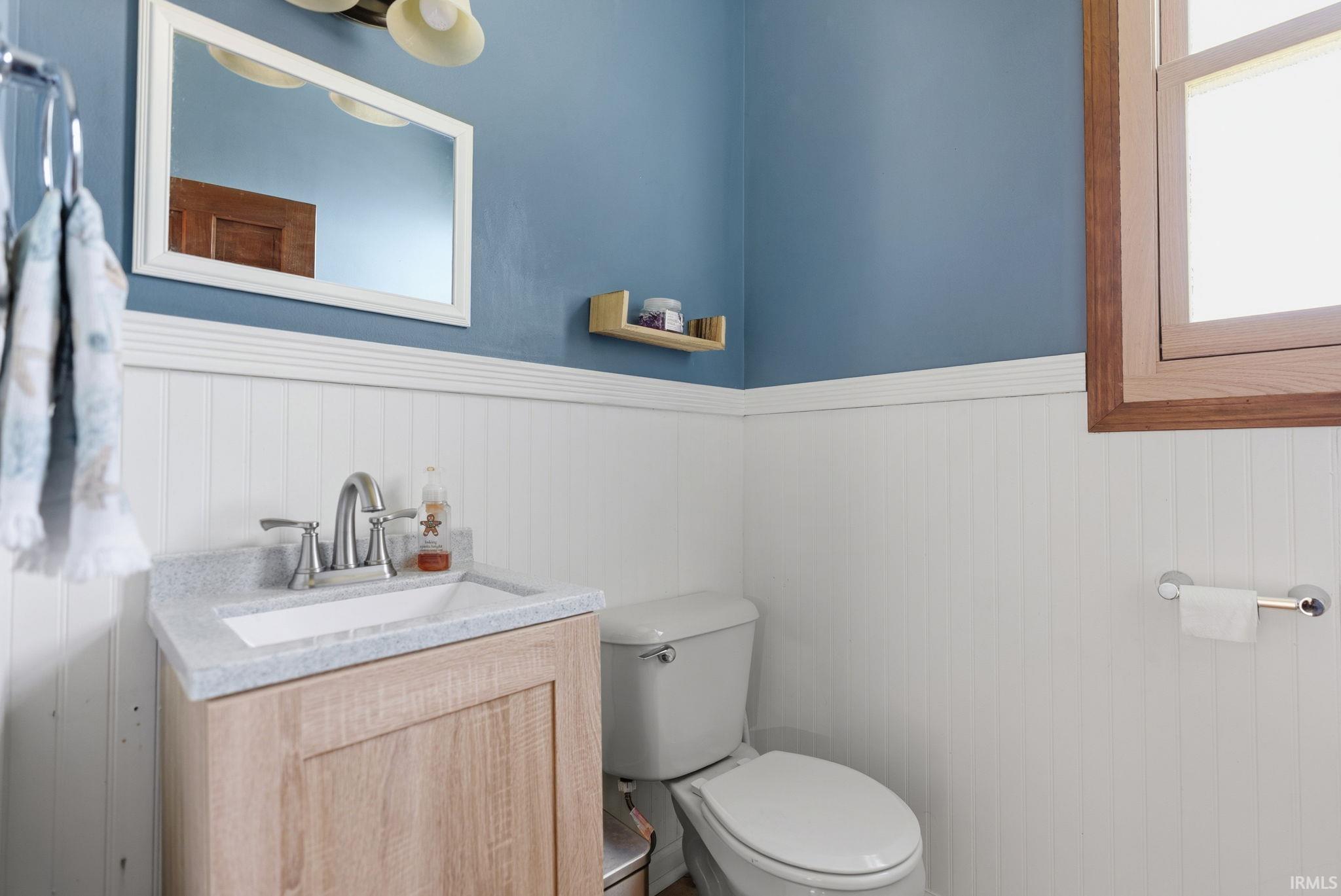 Bathroom featuring a light wood-finish vanity with an integrated sink and brushed nickel faucet, beadboard wainscoting, and a wood-framed window