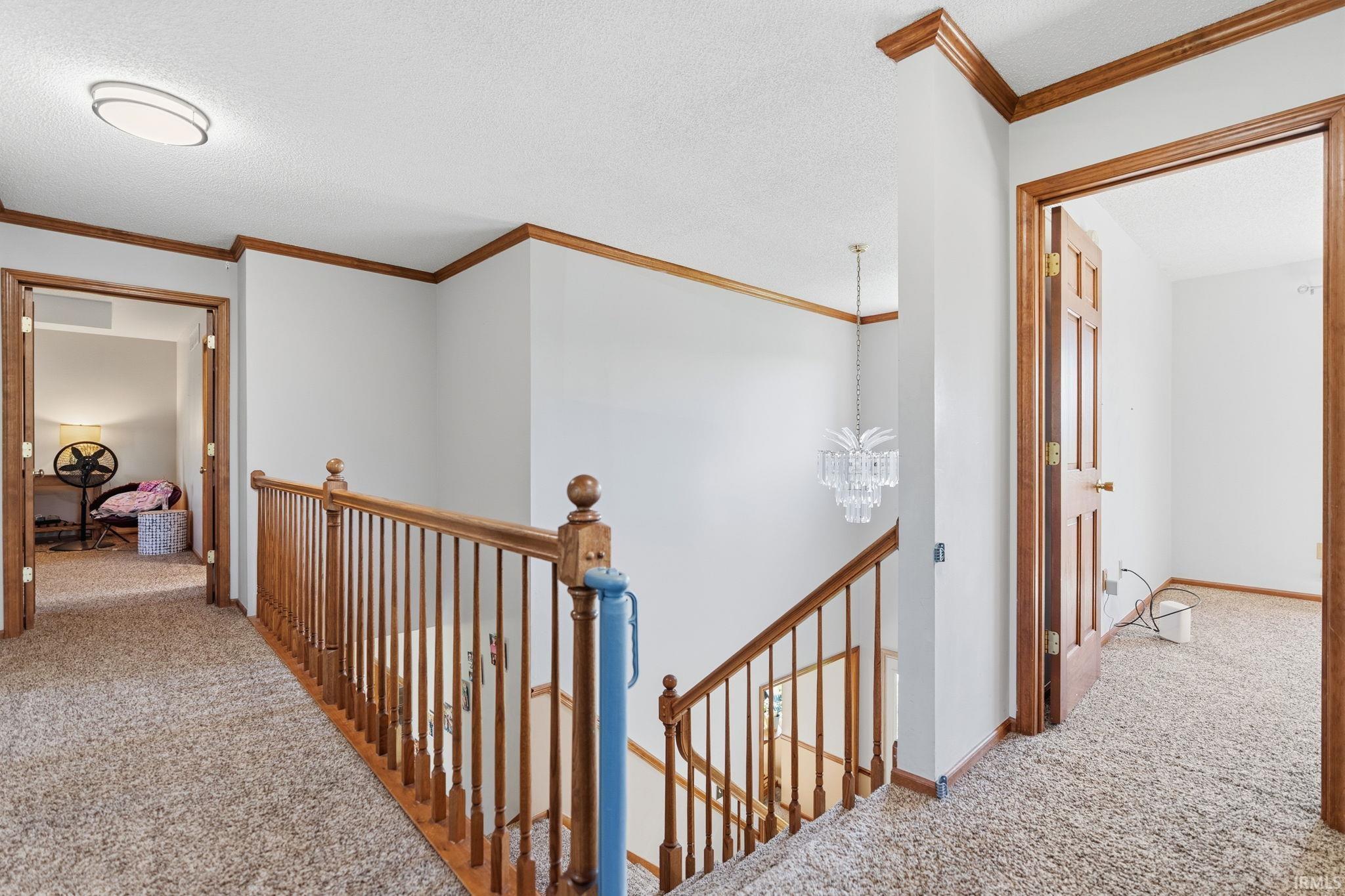 Upper-level landing featuring wood newel posts, balusters, and handrail, complemented by wood doorframes and crown molding