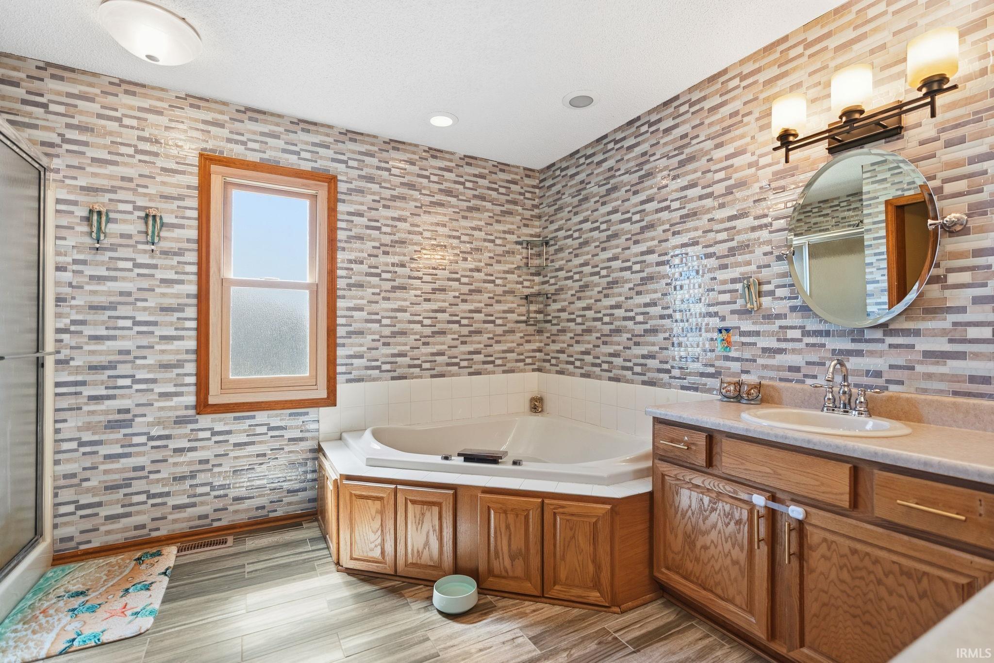 Bathroom featuring a corner soaking tub, a single vanity with wood cabinetry, and a shower enclosure