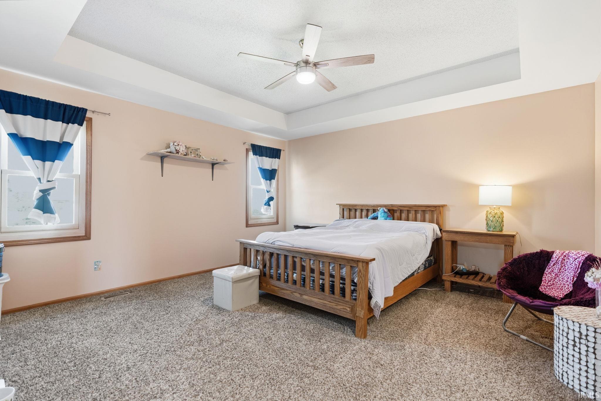 Tray ceiling featuring a contemporary ceiling fan, dual windows with wood trim, and wall-mounted shelving