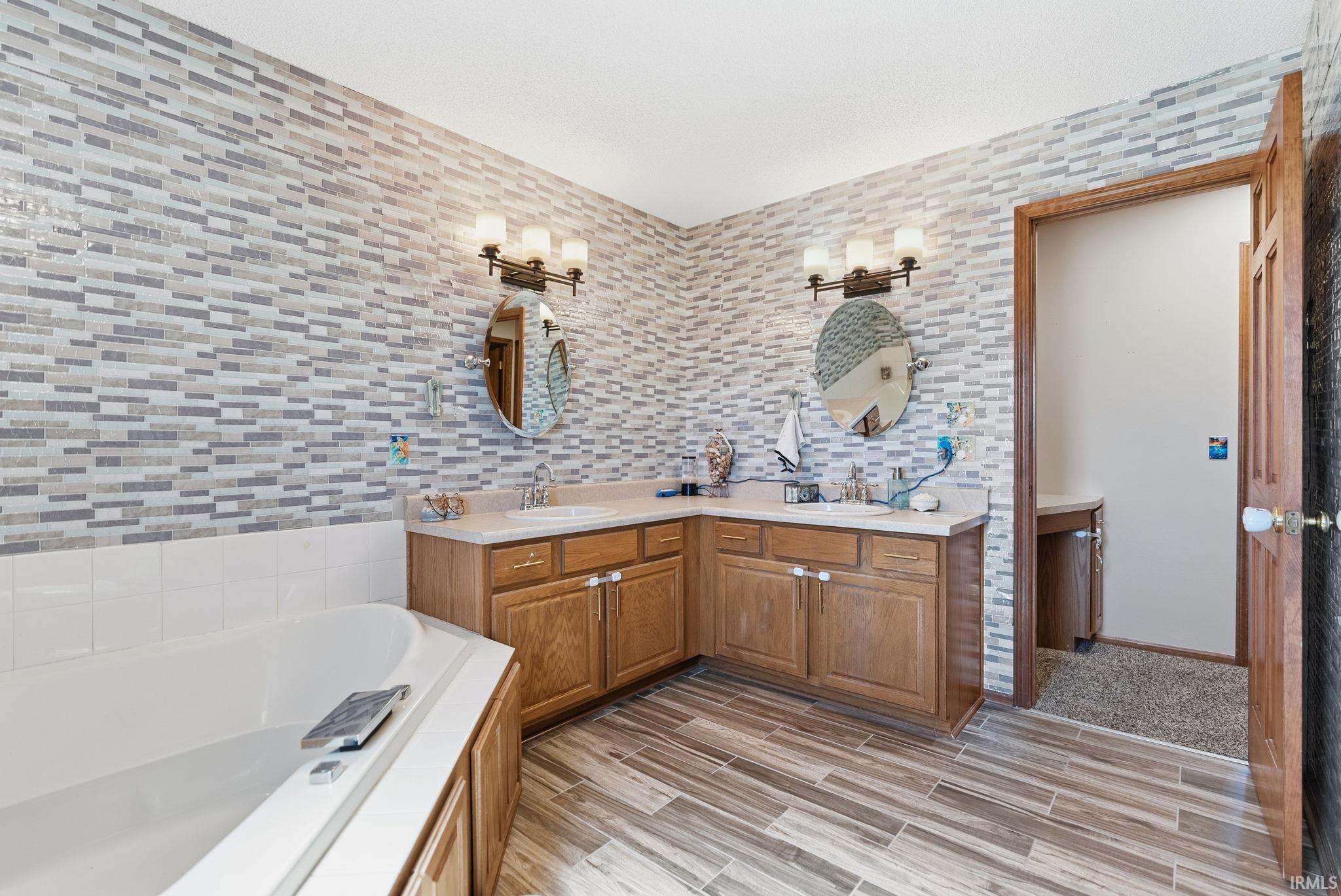 Bathroom featuring wood-finish flooring, a corner soaking tub, and a dual vanity with light-toned countertops