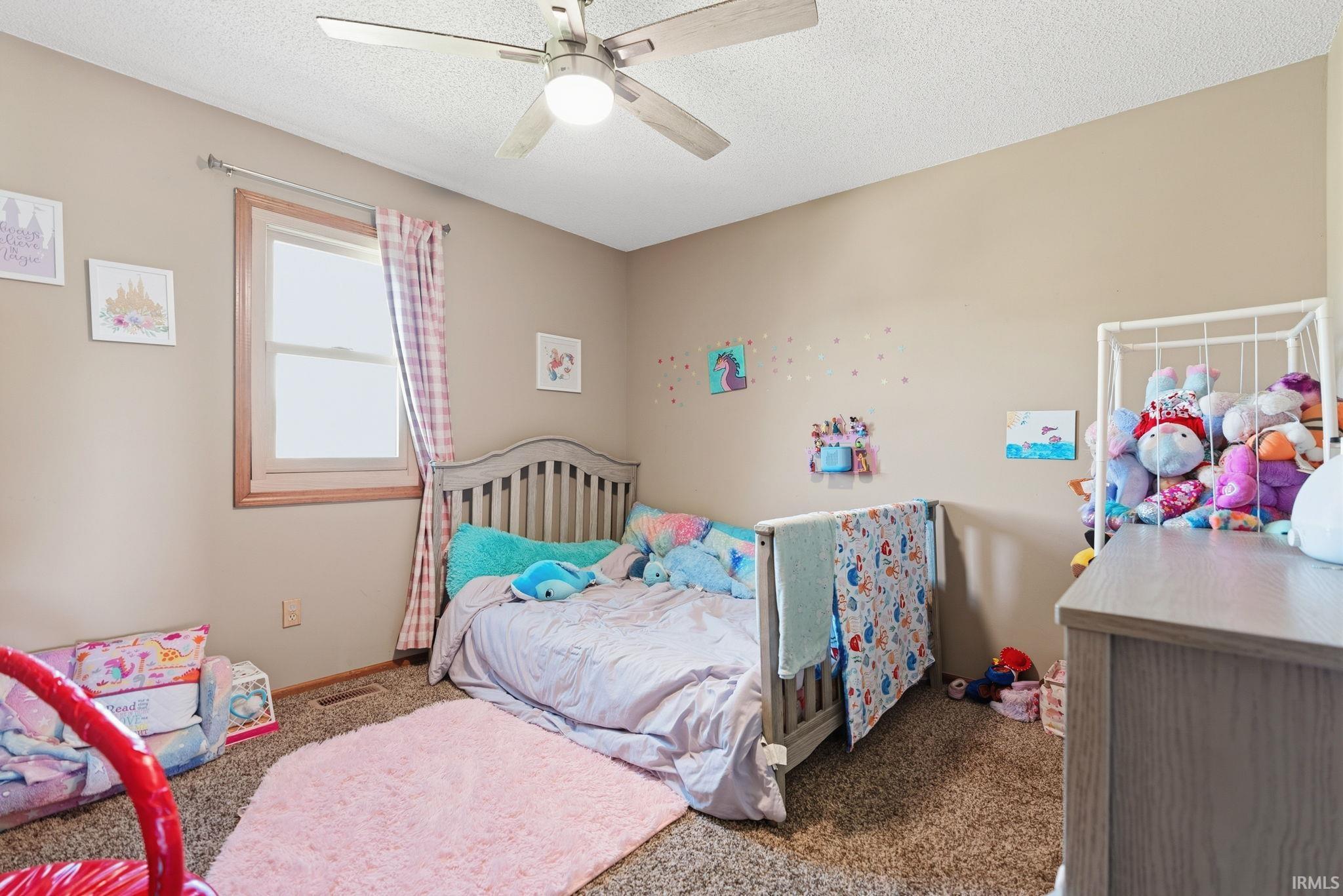 Neutral-toned room featuring a ceiling fan with light fixture, carpeted flooring, and a window with wood trim