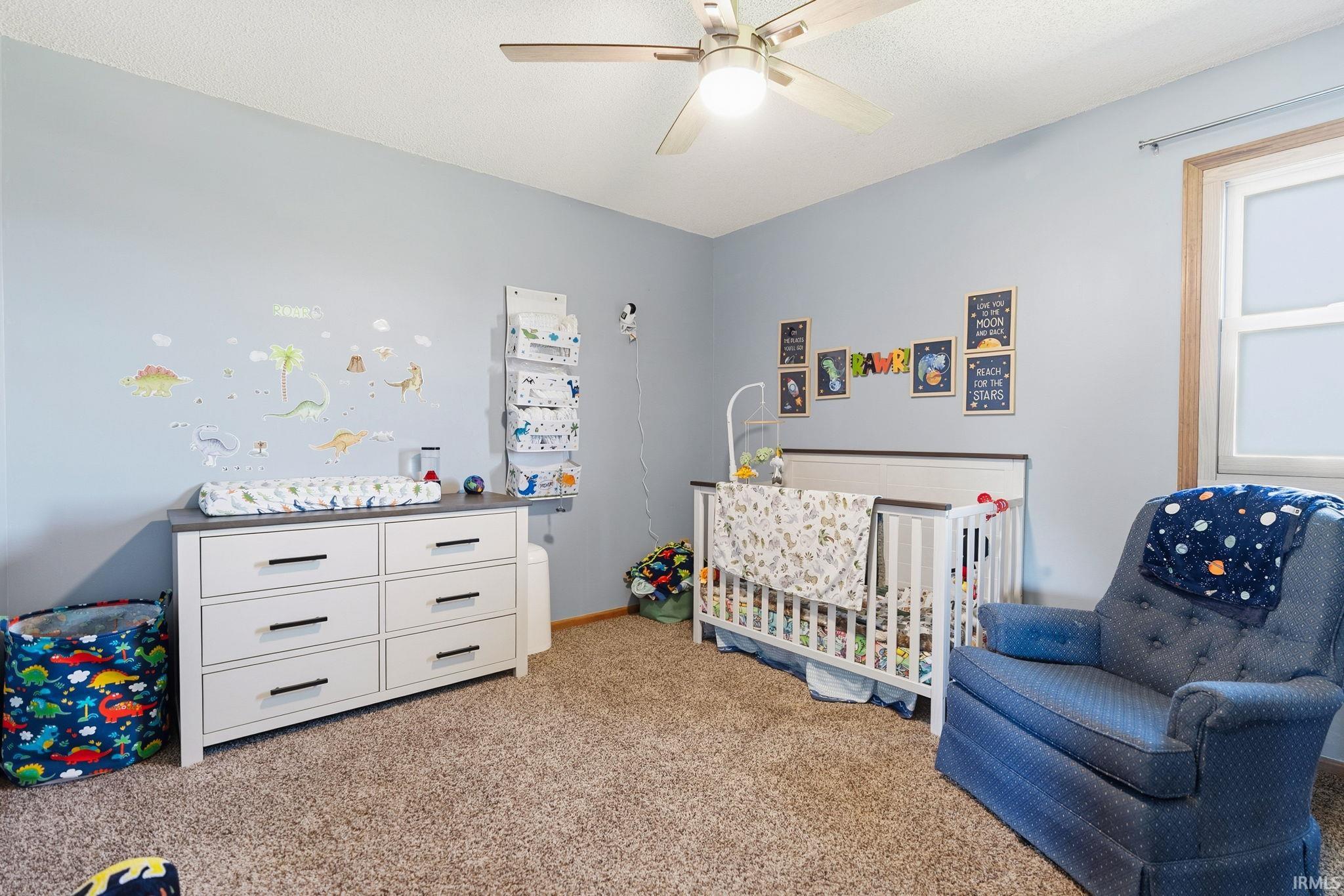 Carpeted room featuring a ceiling fan with integrated lighting, a window with natural wood trim, and light blue wall tones