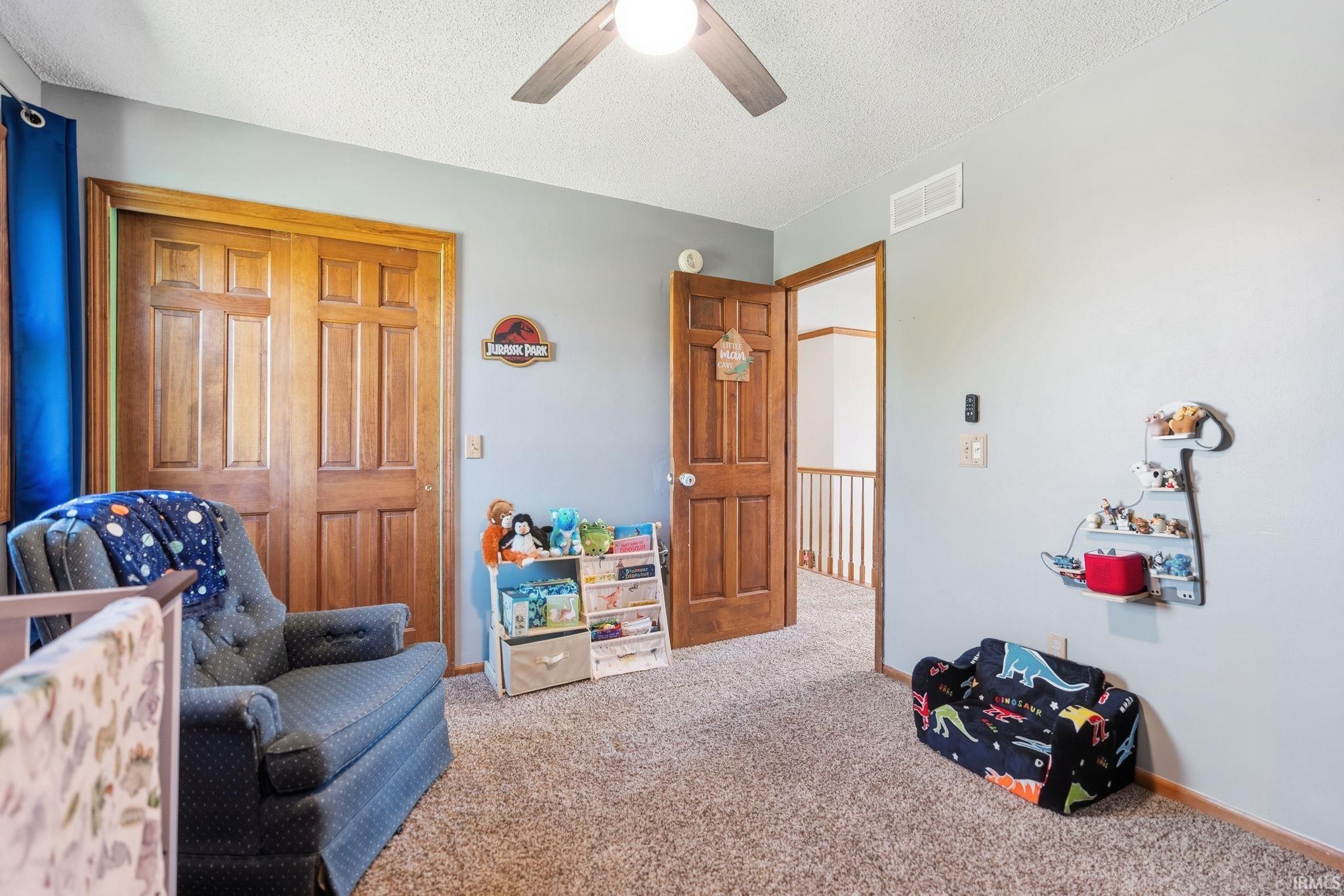 Carpeted room featuring a ceiling fan with light, wood-paneled bi-fold closet doors, and a solid wood door frame