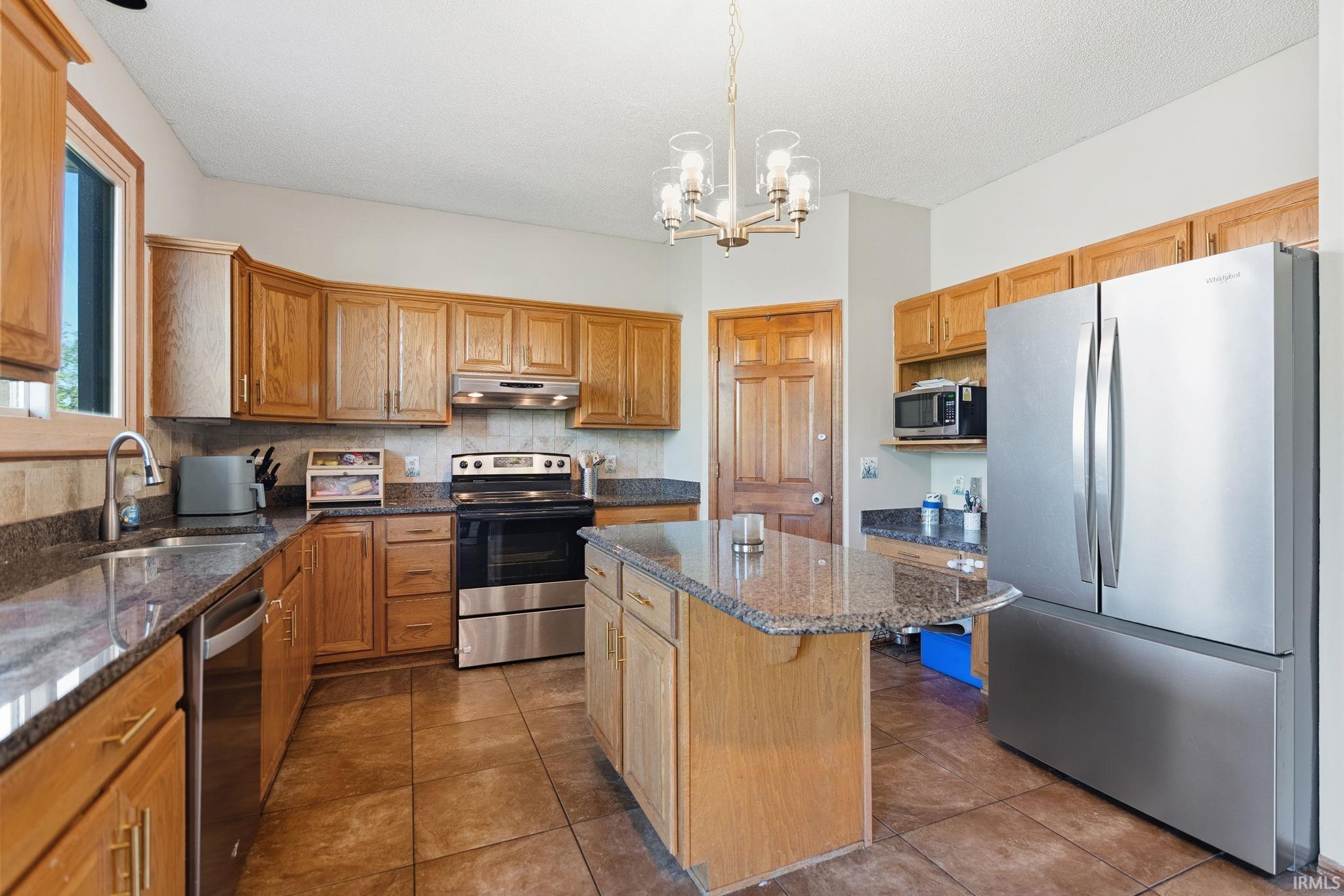 Kitchen featuring a central island with a stone-finish countertop, wood cabinetry, stainless steel appliances, and tile flooring