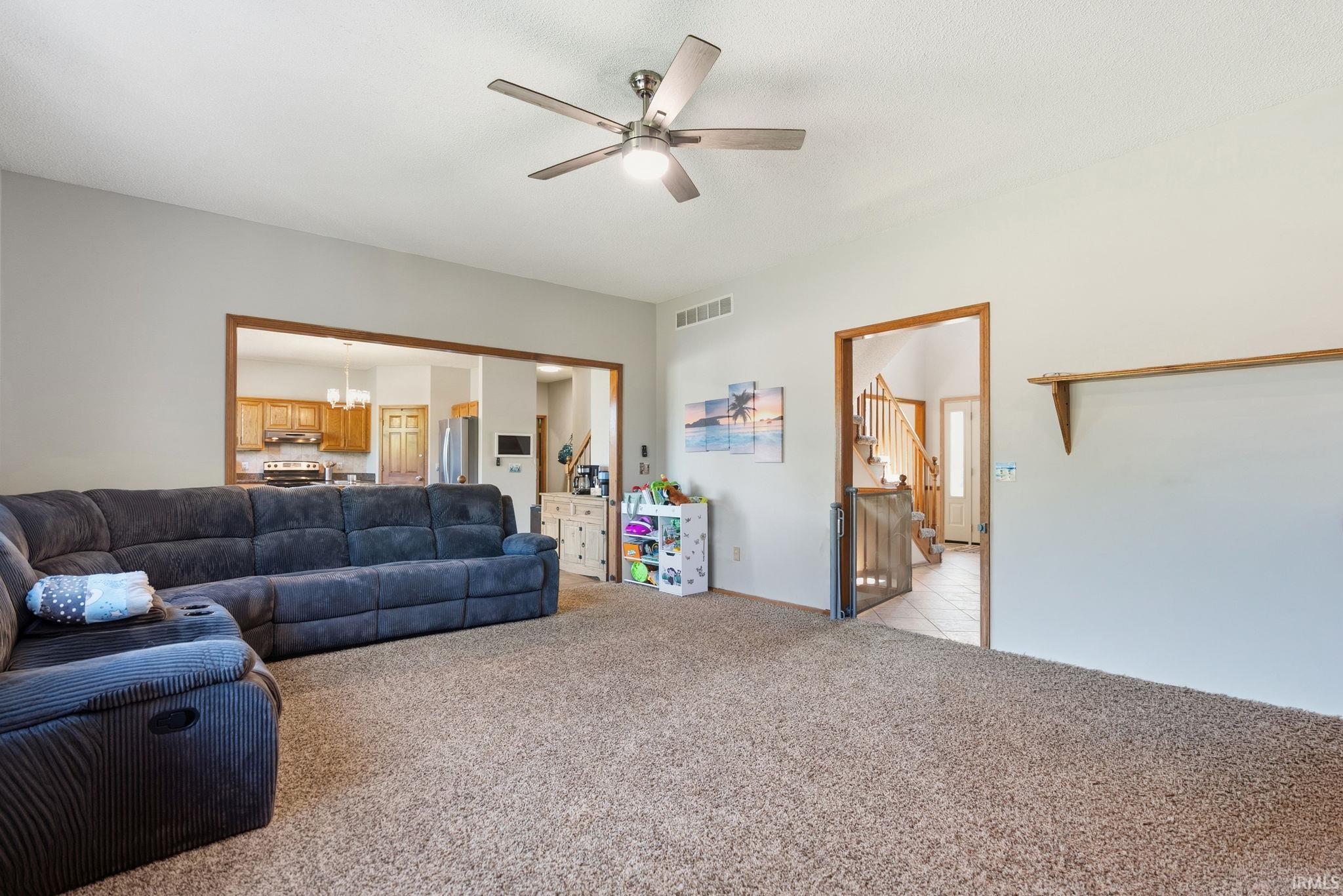 Open-concept living area featuring a neutral carpet flooring, light gray wall paint, and a ceiling fan with integrated lighting