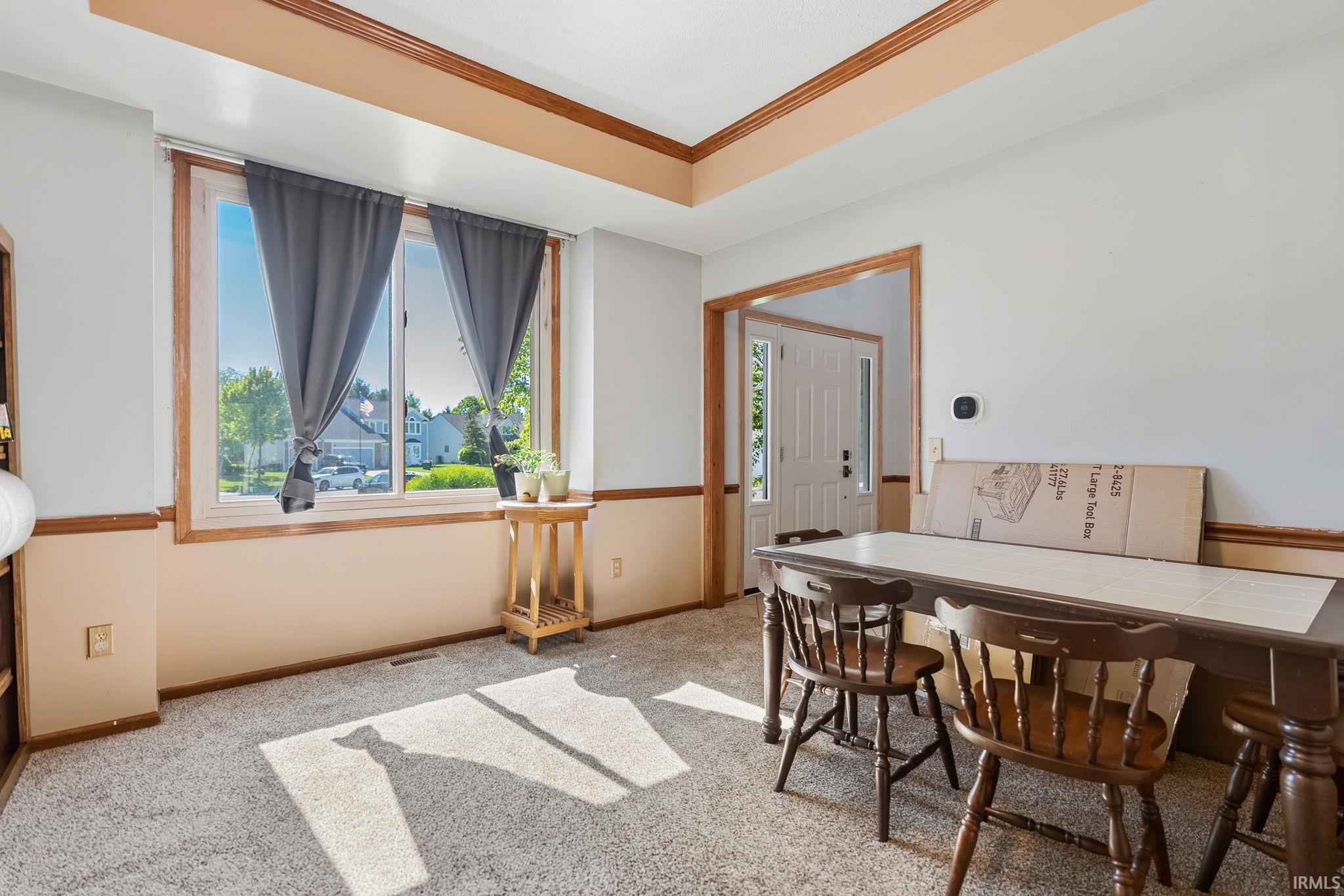 Carpeted room featuring a large window, a tray ceiling, and a doorway opening to a front entry