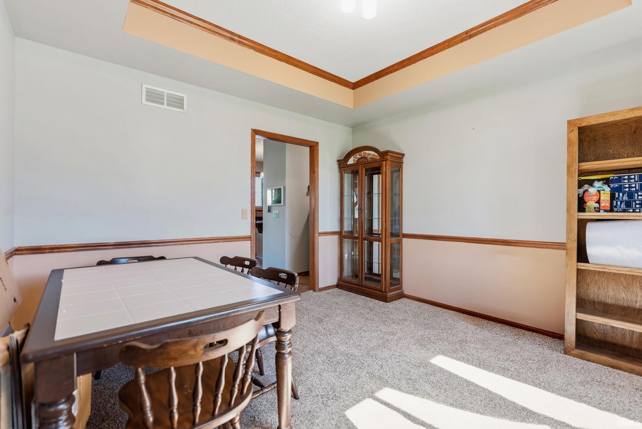 Carpeted room featuring a tray ceiling with wood trim, two-tone painted walls with wood trim, and a doorway with wood casing