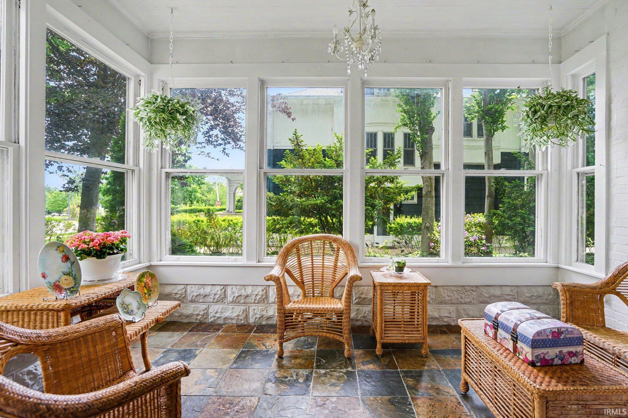 Sunroom featuring a multi-pane window wall, white trim, stone tile flooring, and a crystal chandelier