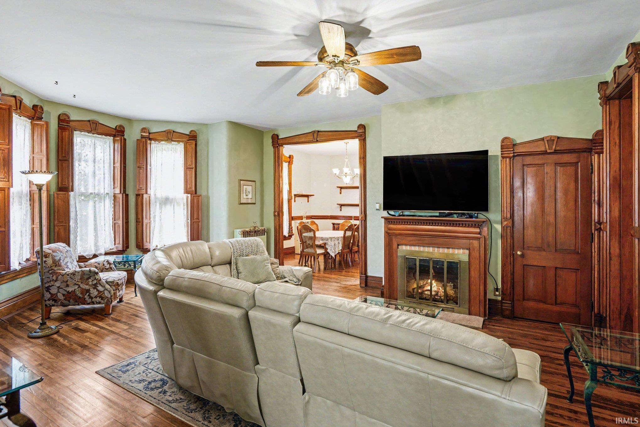 Living area featuring hardwood flooring, a ceiling fan with integrated lighting, and a decorative fireplace with a wood mantel
