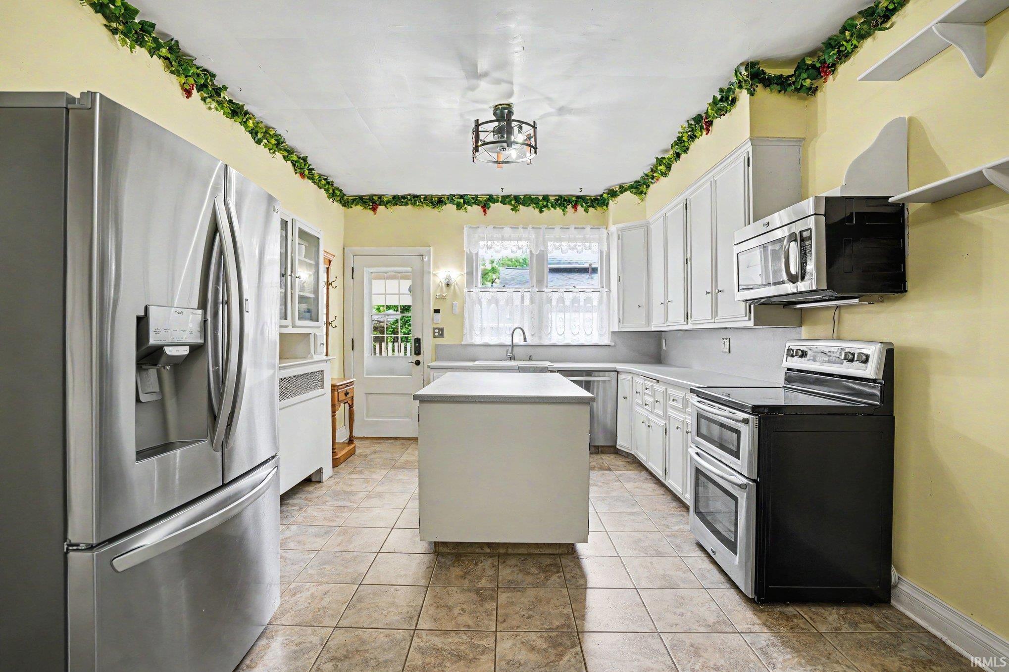 Kitchen featuring a central island, stainless steel refrigerator, white cabinetry, integrated sink, and tile flooring