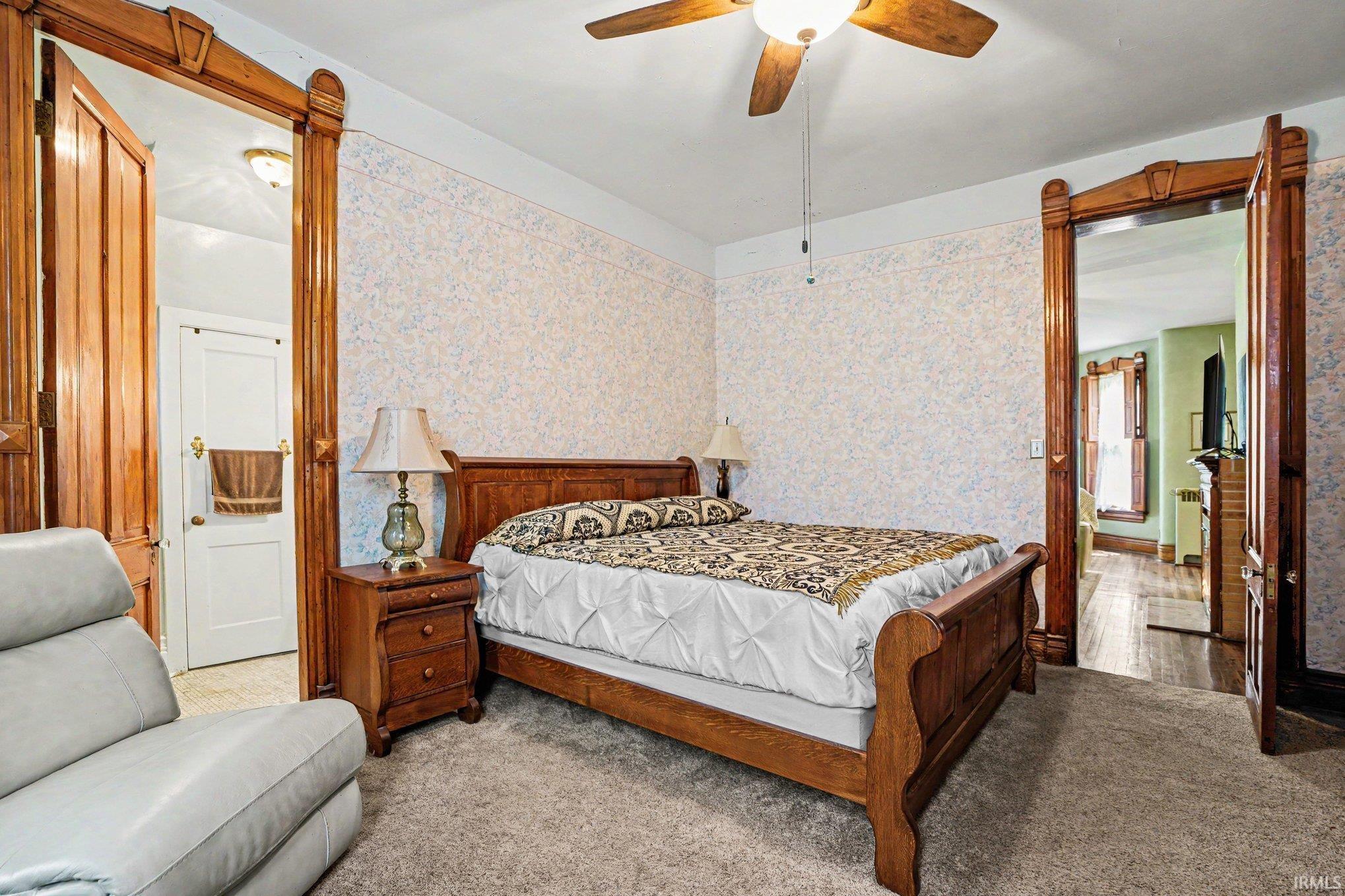 Originally the billiard room..currently being used as main floor master bedroom with connecting half bath...Room featuring patterned wallpaper, carpeted flooring, and a ceiling fan with integrated lighting