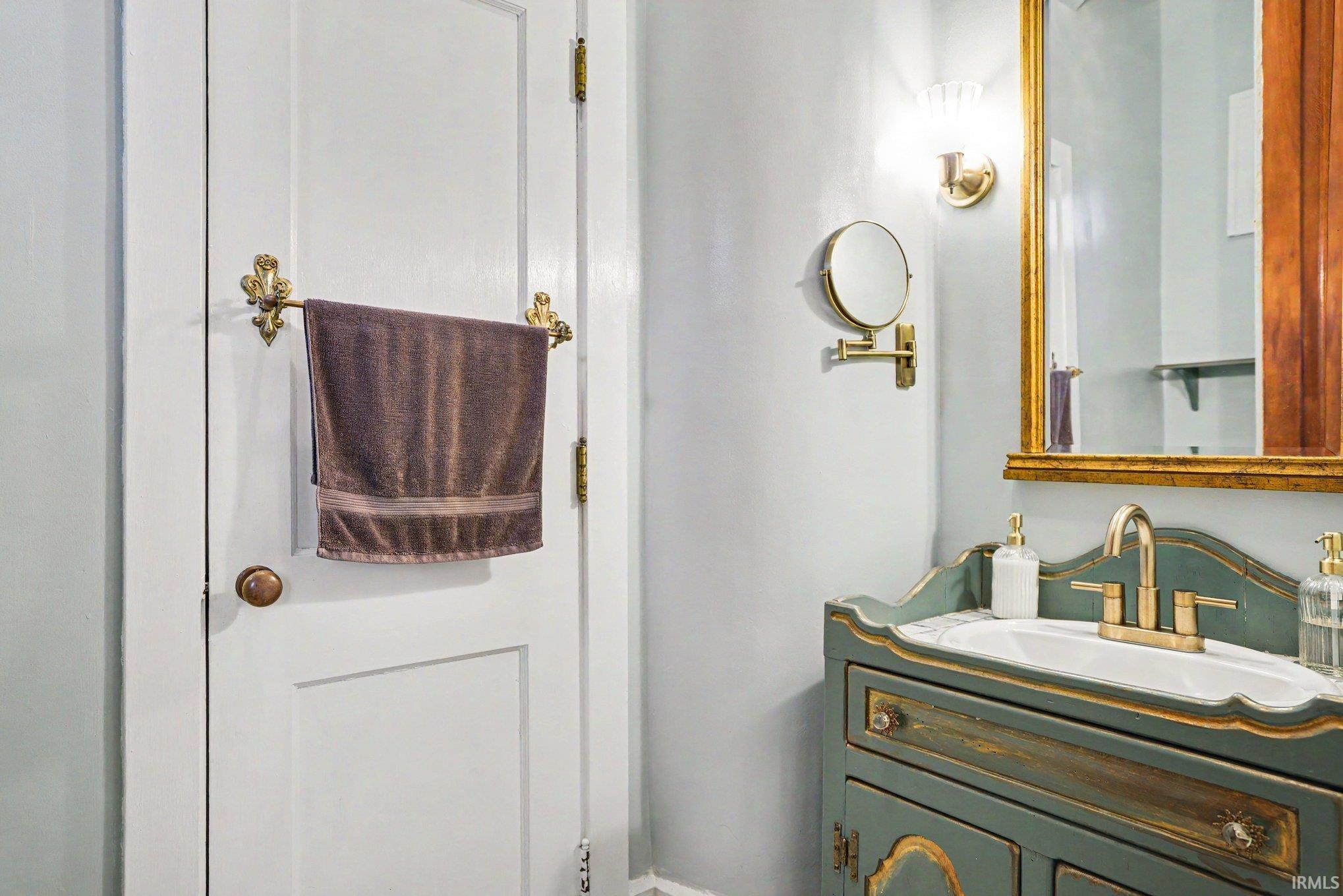 Main floor half bath ensuite connected to main floor master bedroom with ornate vanity featuring a sink with a gold-tone faucet, framed by a gold-tone mirror and wall sconce