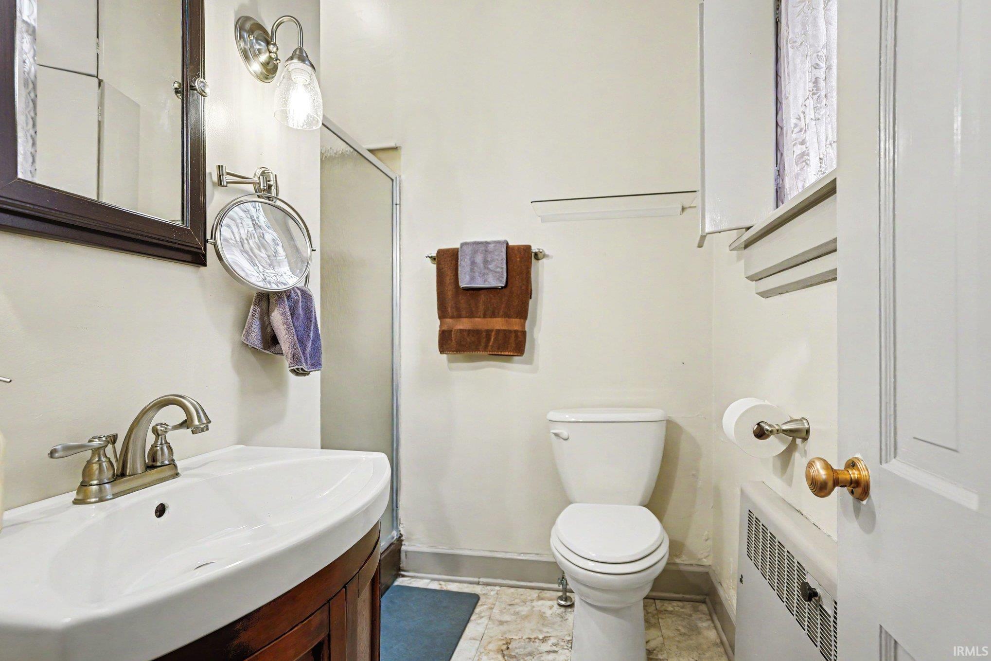 Main floor full bathroom ensuite to second bedroom featuring a wood-finish vanity with a curved basin sink, a brushed nickel faucet, a frameless shower enclosure, and neutral-toned flooring