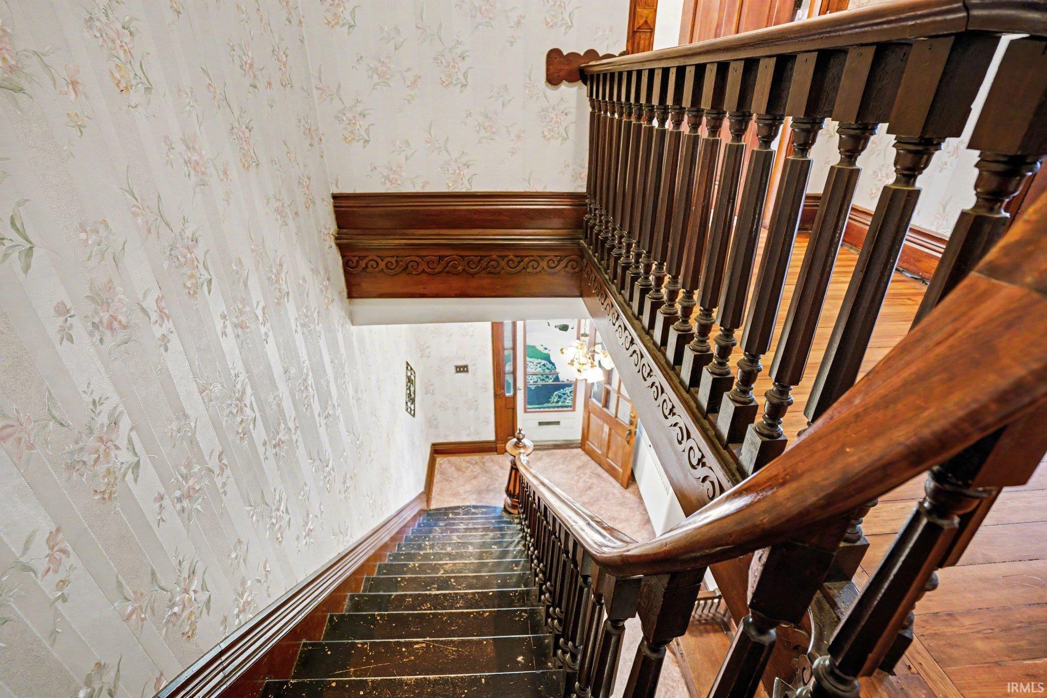 Ornate wood staircase with balusters and carved newel posts, featuring a dark wood-finish handrail