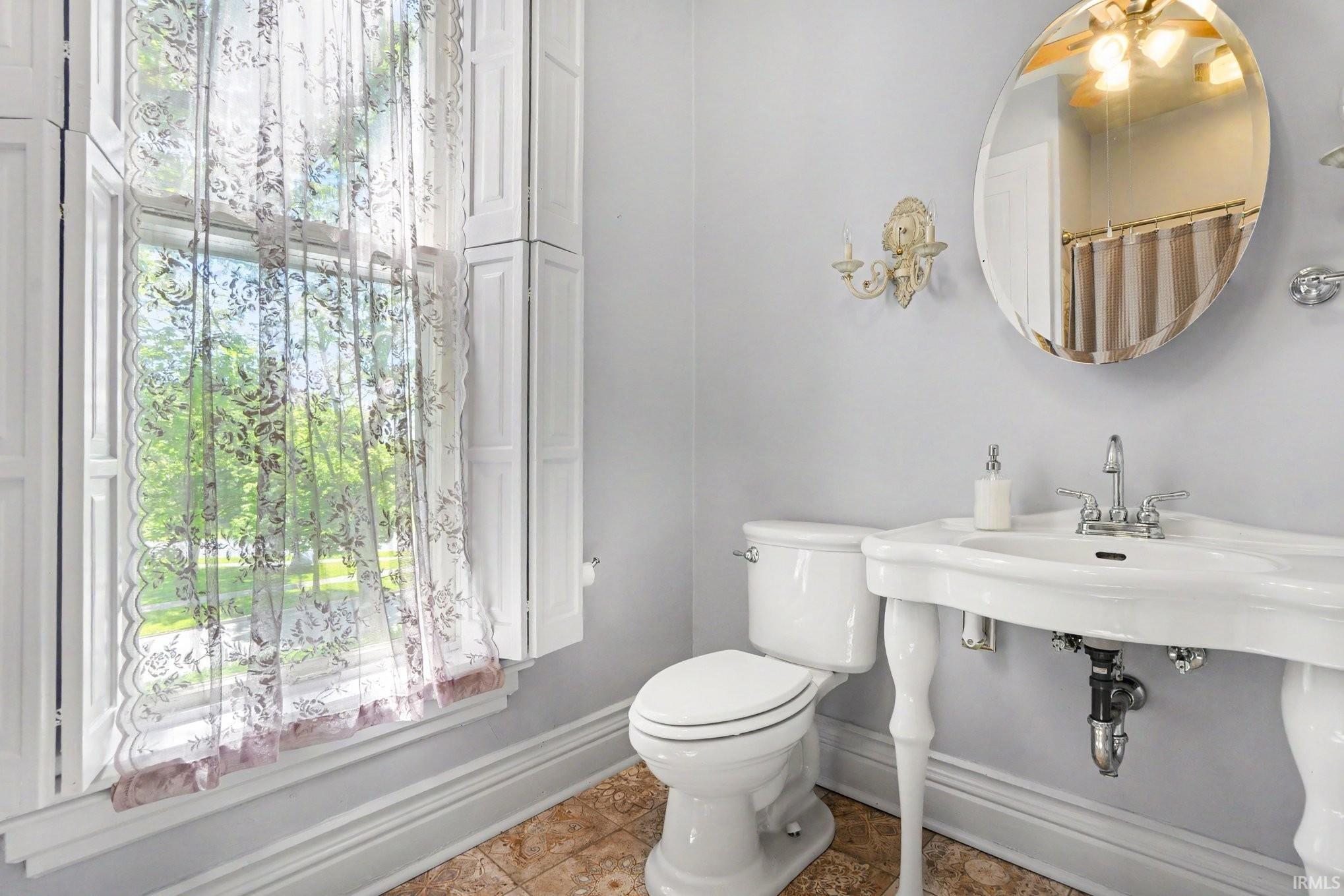 Second full Bathroom upstairs featuring a pedestal sink, oval mirror, wall sconce lighting, and a window with plantation shutters