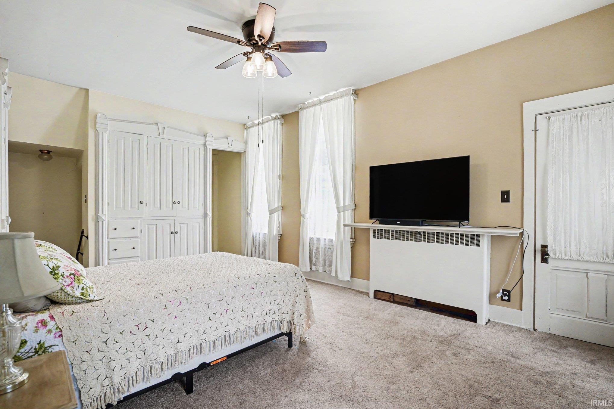 Upstairs bedroom with attached full bath described as the servant quarters, carpeted room with a built-in white cabinetry unit, a ceiling fan, and two windows with white curtains