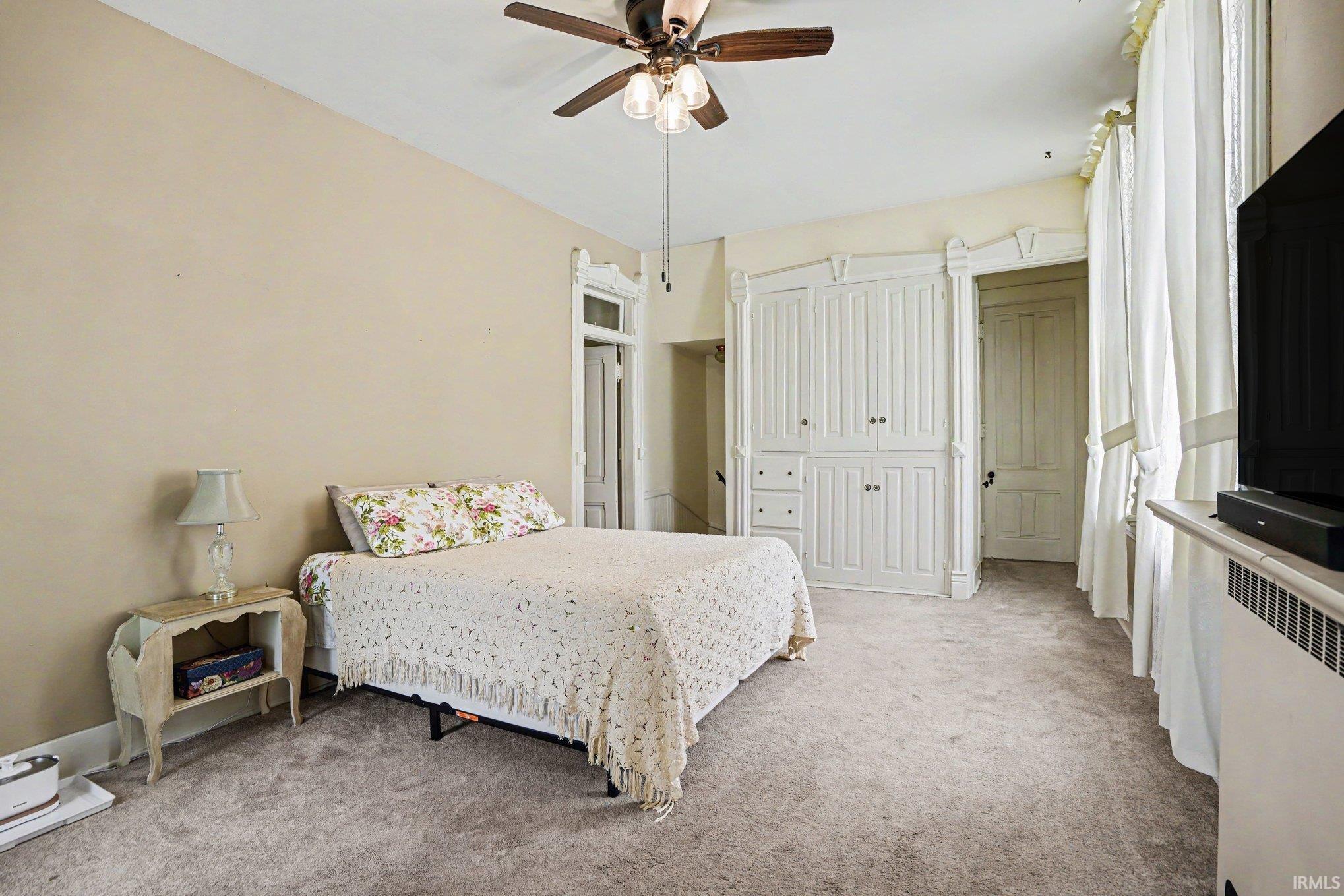 Upstairs bedroom with attached full bath described as servant quarters. Neutral-toned room featuring a ceiling fan with light kit, built-in cabinetry with paneled doors and drawers, a traditional paneled door with transom, and carpeted flooring