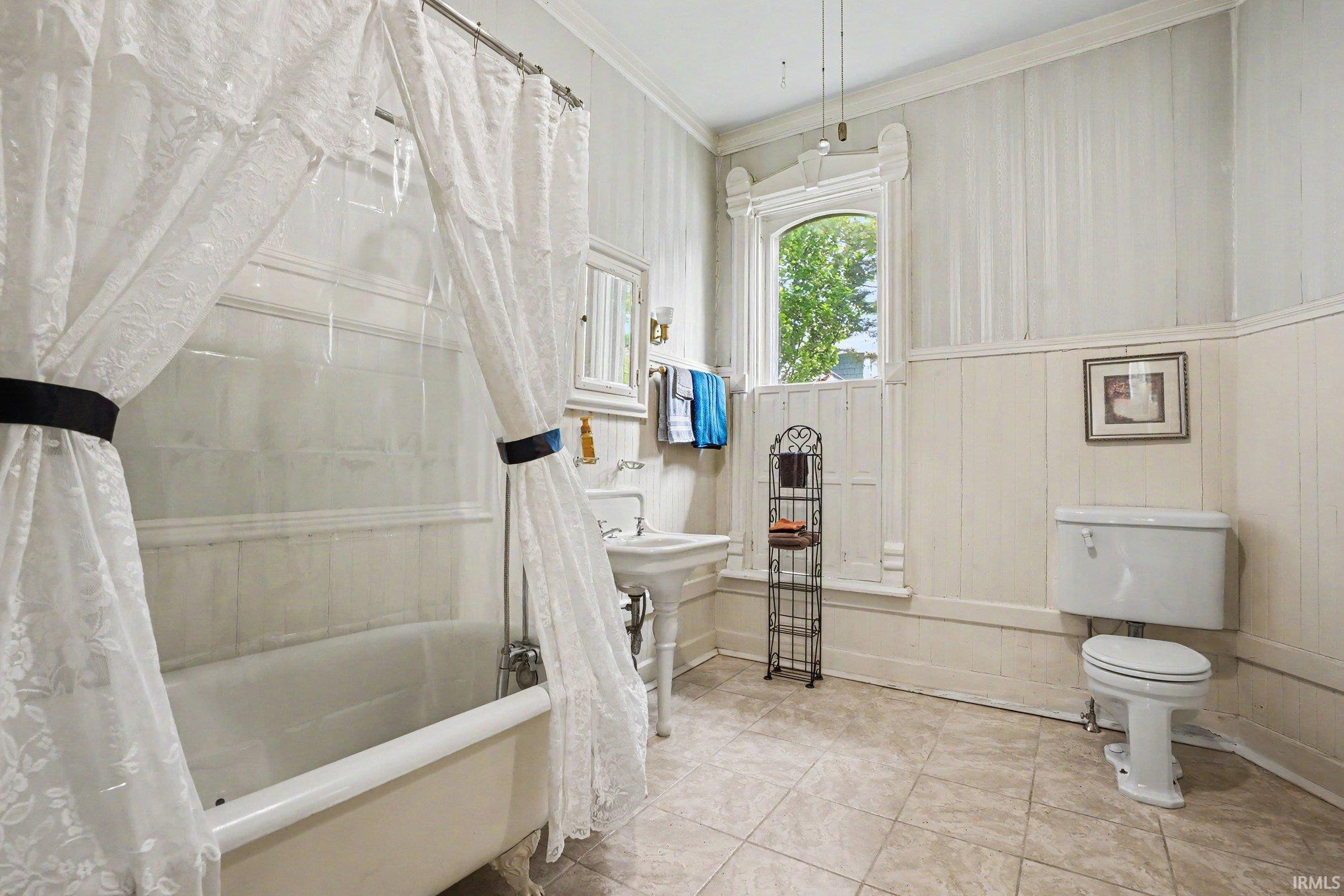 Upstairs full bathroom ensuite attached to a upstairs bedroom featuring a clawfoot tub, pedestal sink, and tiled flooring. Originally the 'maid quarters'.