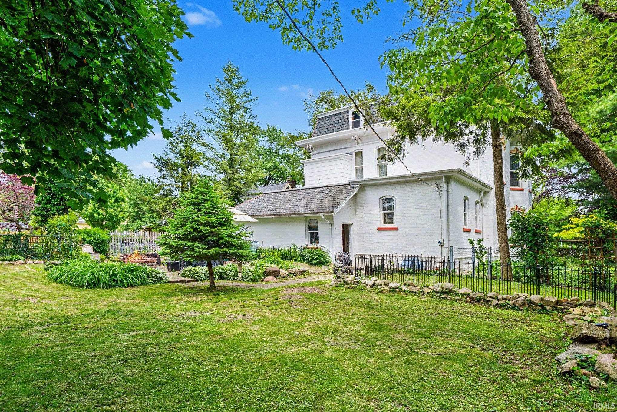 Expansive rear yard featuring a manicured lawn, established landscaping, and mature trees