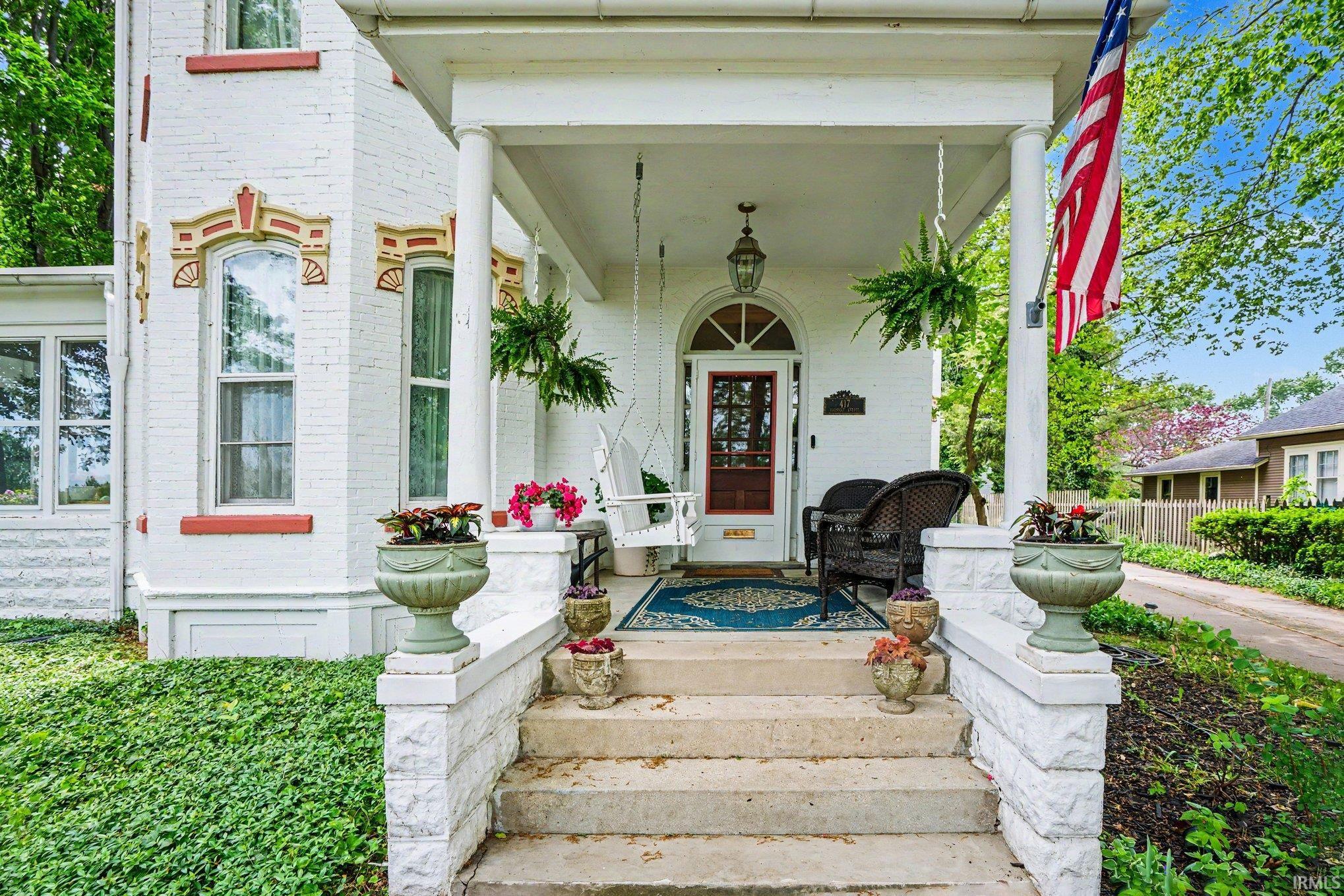 Covered front porch with white columns, concrete stairs, and a visible front entry door featuring an arched transom window