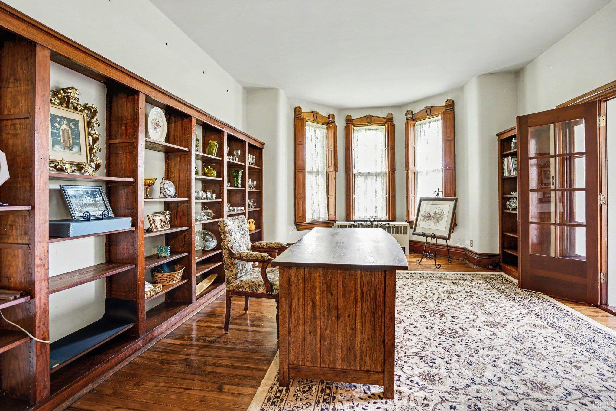 Room featuring extensive built-in wooden shelving, a bay window with wood-trimmed frames, wood-finish flooring, and a glass-paneled wooden door