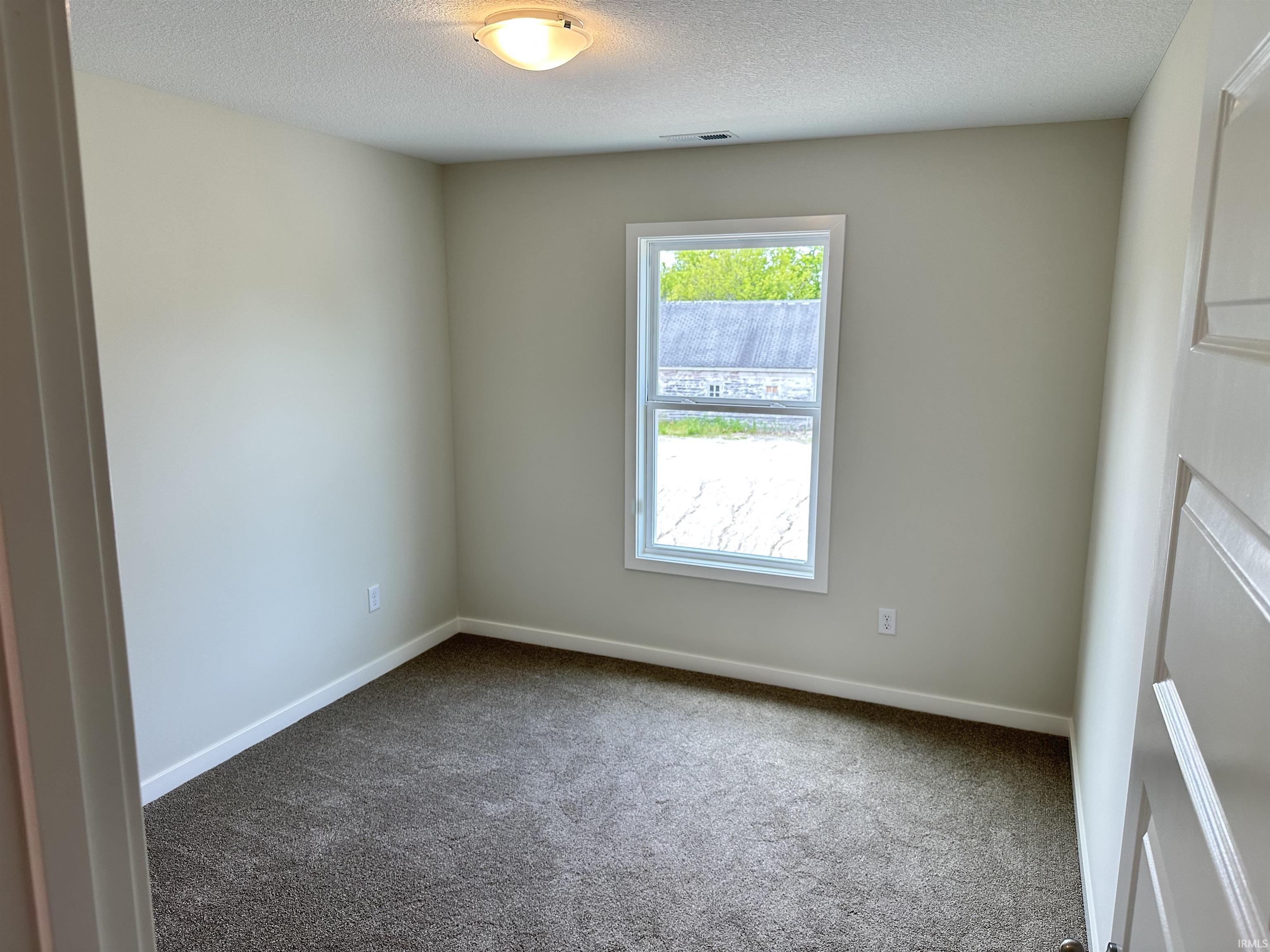 Bedroom featuring neutral wall paint, textured carpeting, white trim, and a double-pane window