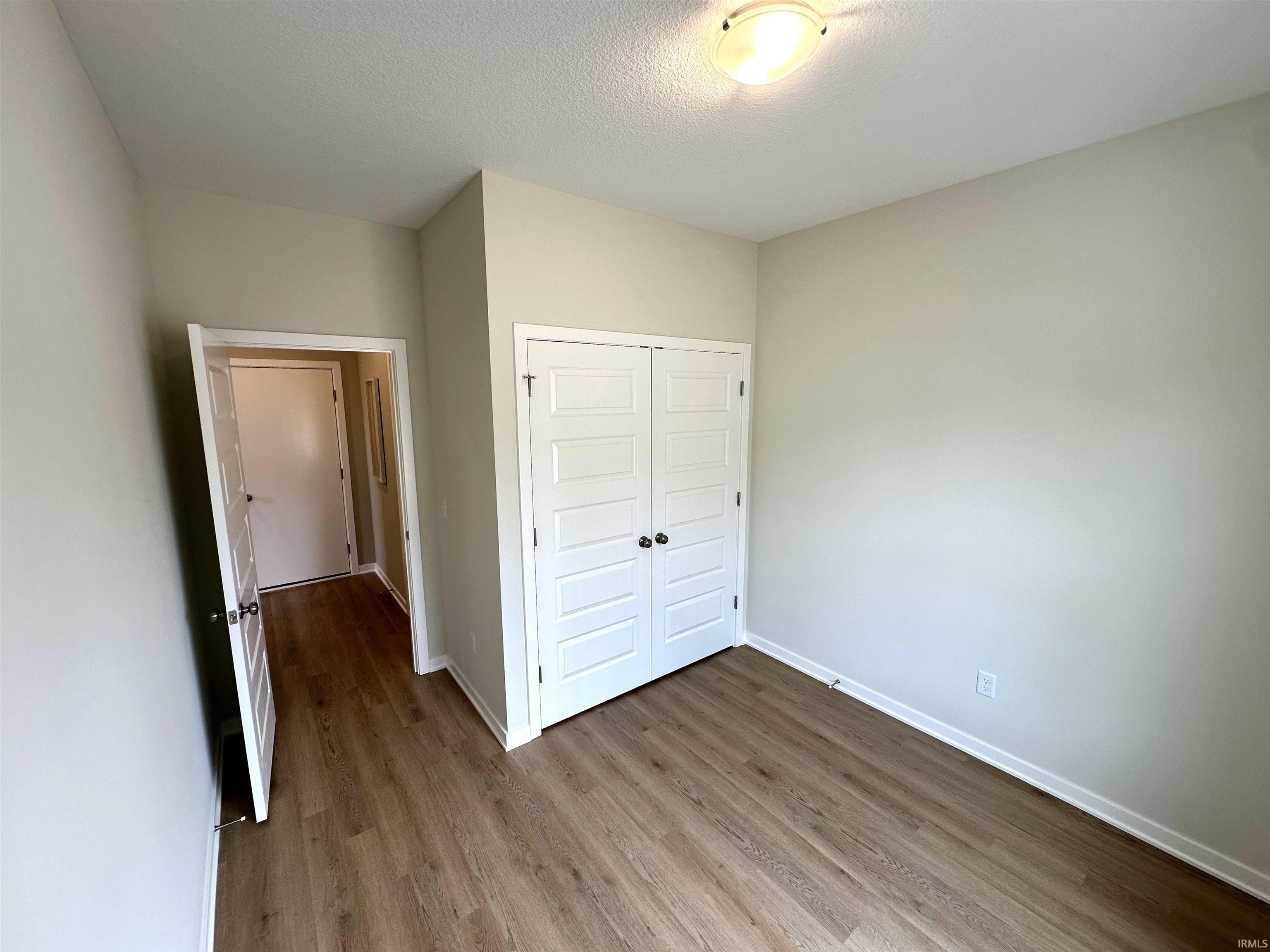 Interior room featuring wood-finish flooring, light-toned wall paint, white baseboards, and a white paneled bi-fold closet door