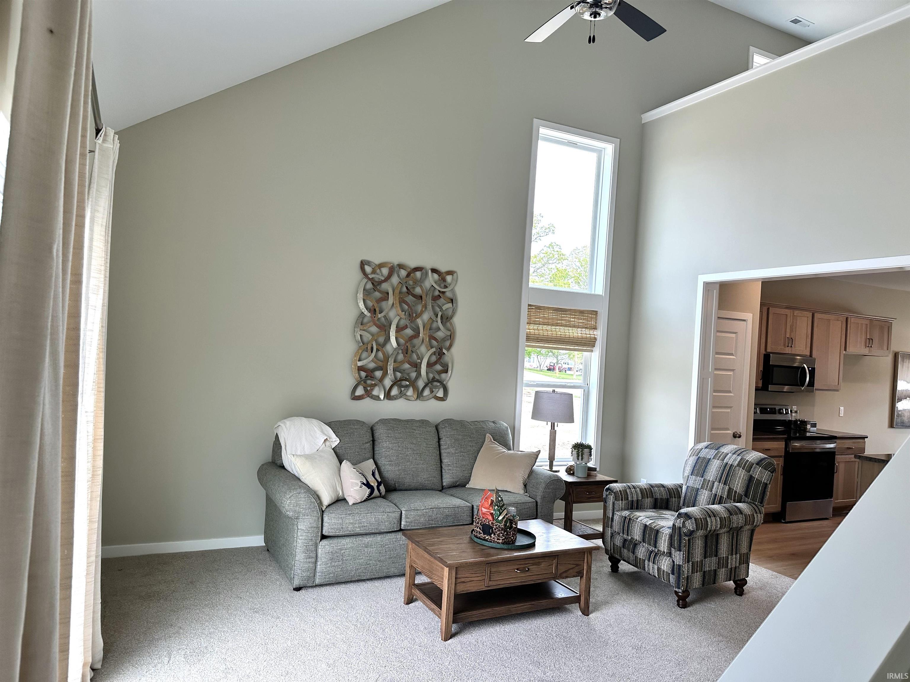 Vaulted ceiling living space featuring a ceiling fan, a tall vertical window, and carpet flooring
