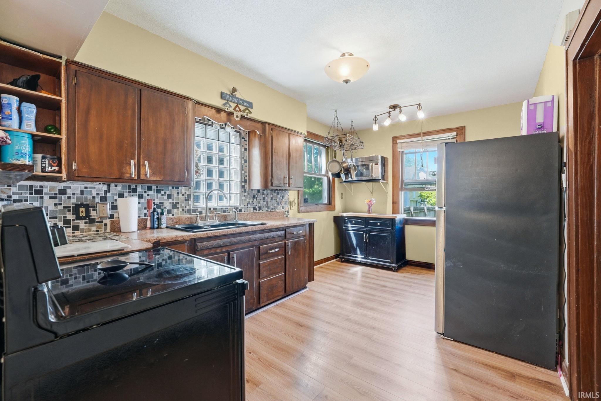 Spacious kitchen featuring wood-finish flooring, dark wood cabinetry, a decorative tile backsplash, and a built-in electric range