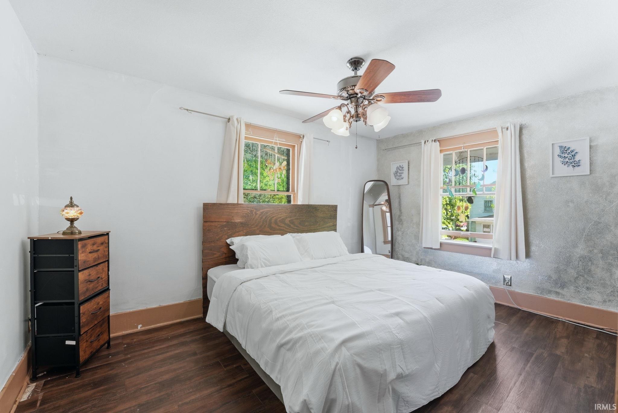 Bedroom featuring dark wood-finish flooring, a ceiling fan with integrated lighting, and two windows providing natural light