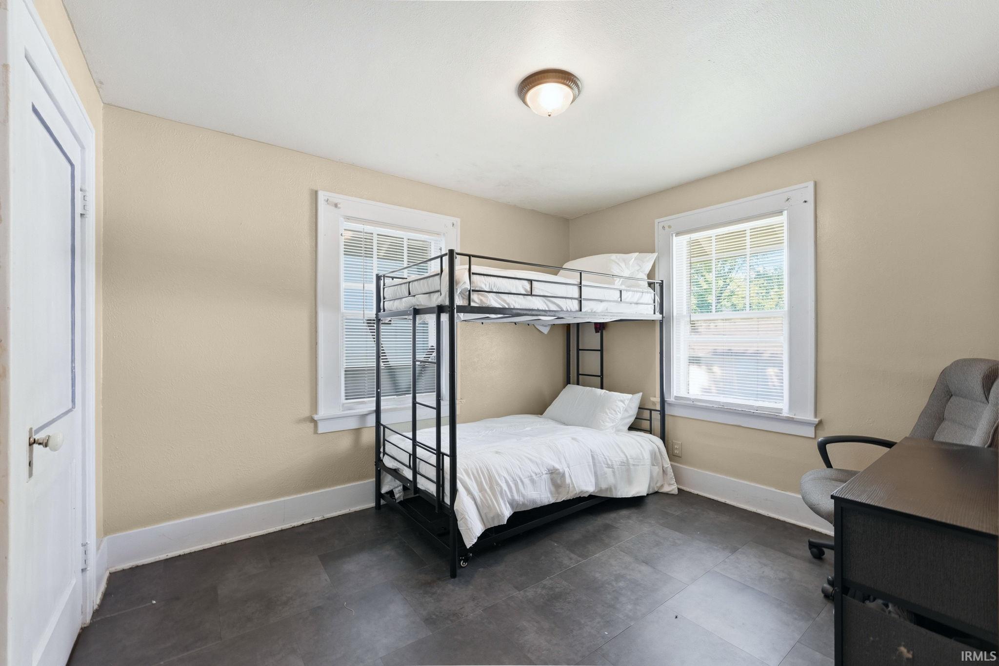 Neutral-toned walls complement the dark flooring in this room featuring two windows with white trim and a ceiling-mounted light fixture