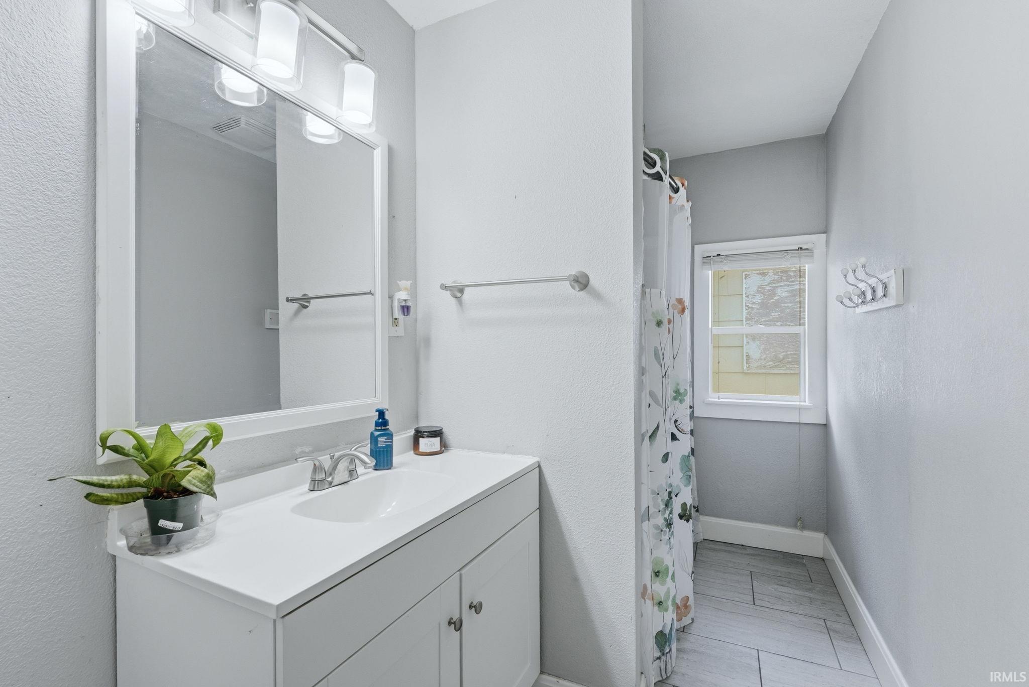 Bathroom featuring a white vanity with integrated sink, chrome faucet, framed mirror, and overhead light fixture