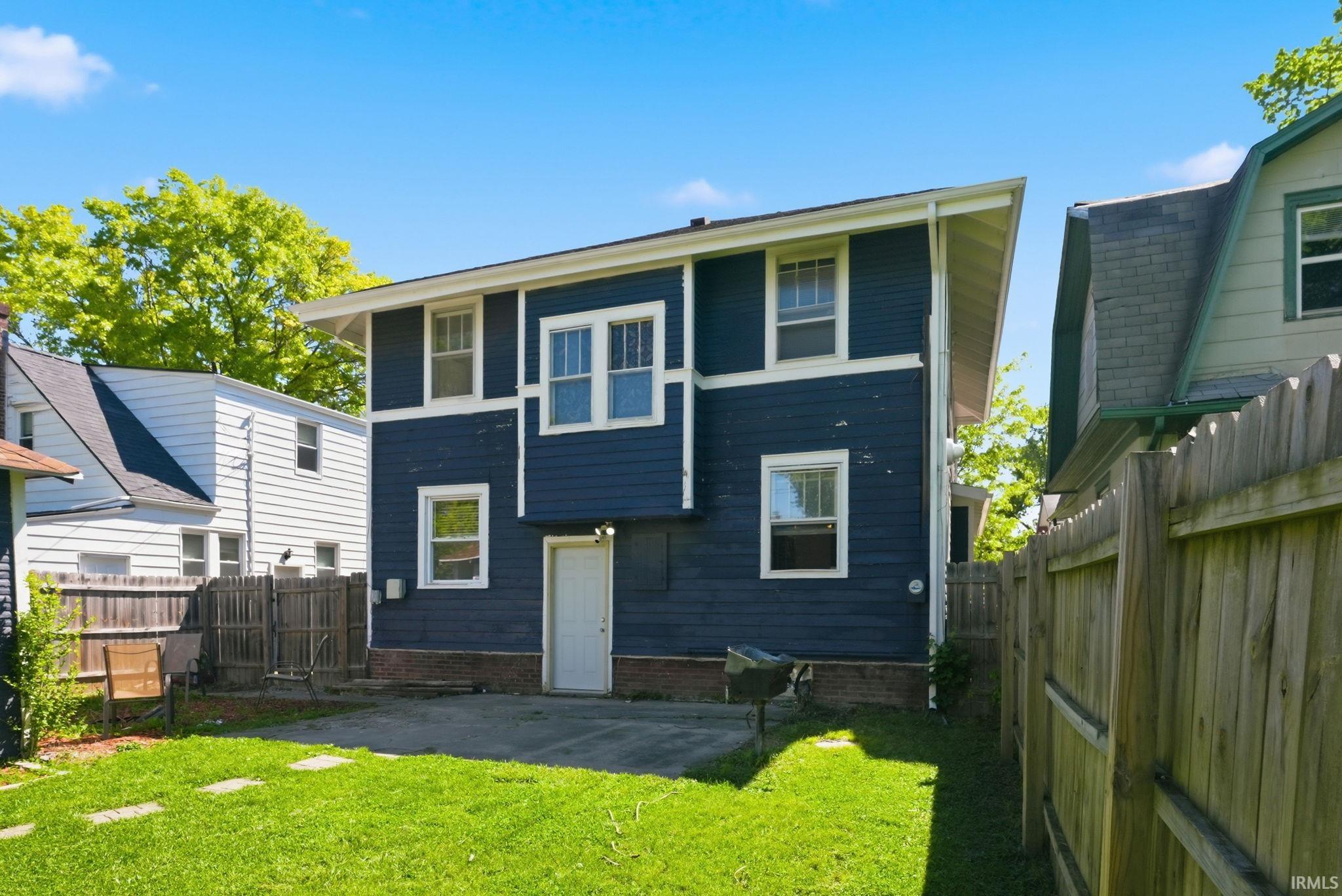 Rear exterior featuring dark blue siding with white trim, multiple windows, and a ground-level door