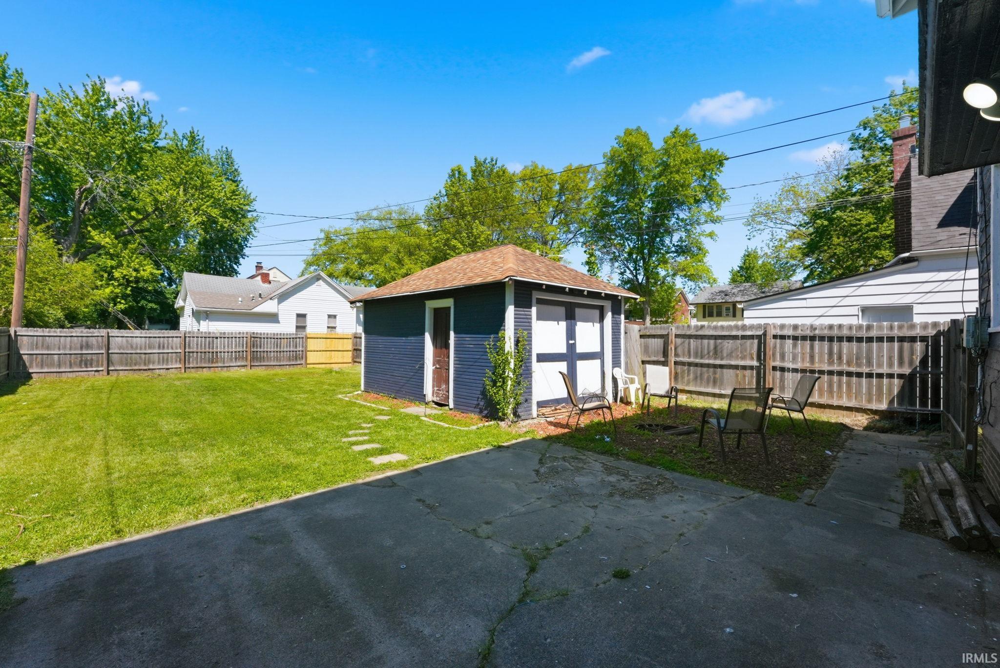 Spacious backyard featuring a detached garage with a brown shingle roof, a concrete patio area, and a large grassy expanse