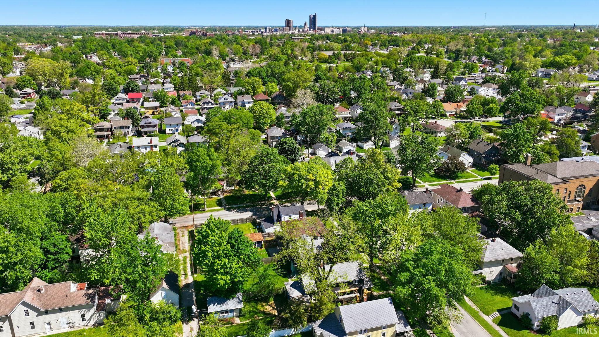 Aerial perspective showcasing a residential neighborhood with abundant mature trees and a distant skyline