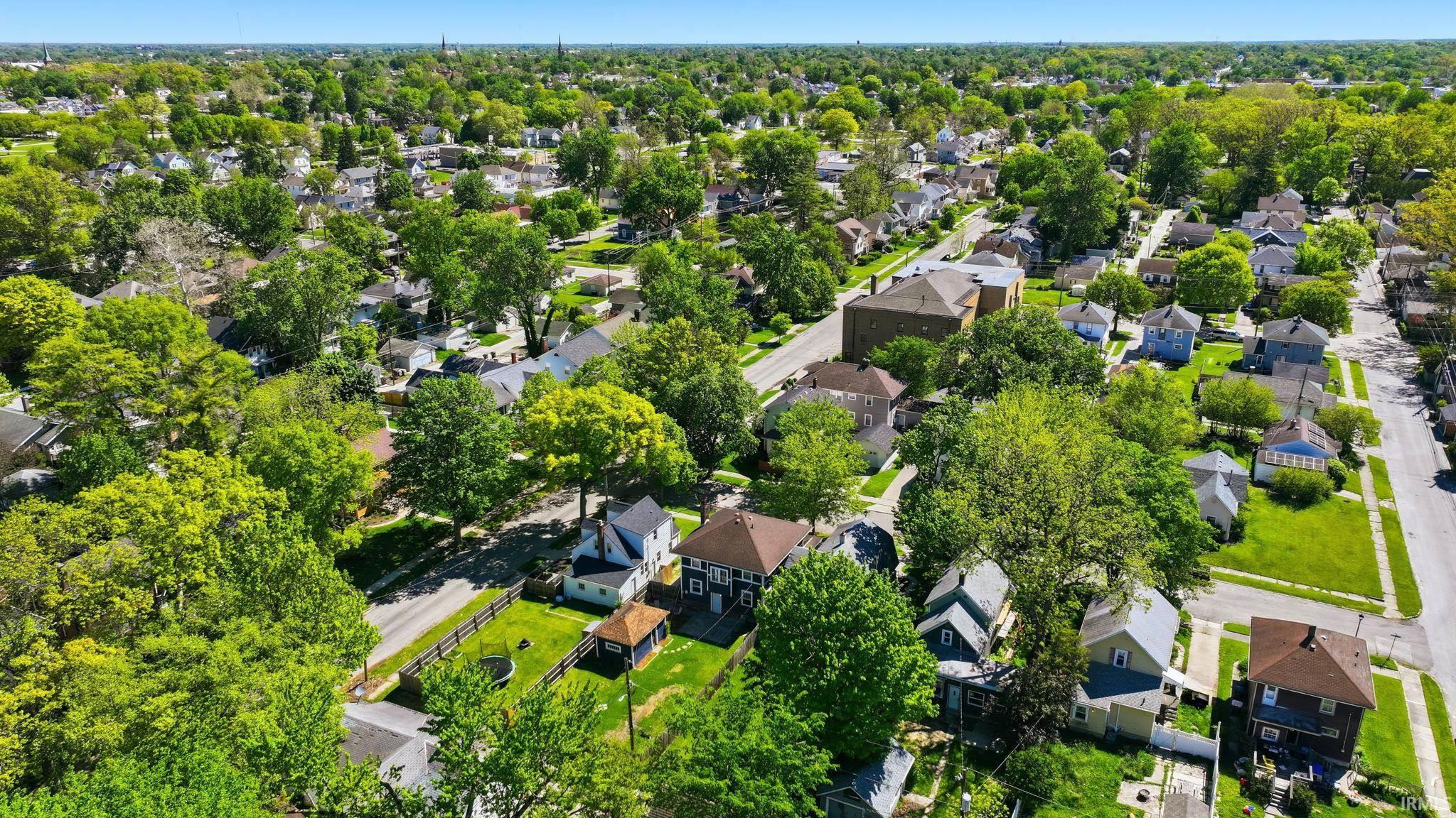 Aerial perspective of a residential neighborhood featuring established trees, individual homes with varying architectural styles, paved streets, and green spaces
