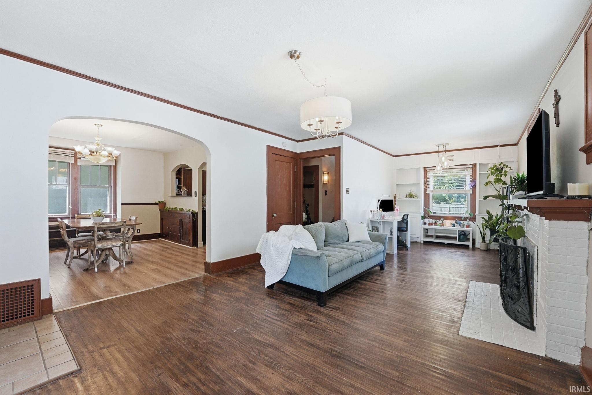 Spacious living area featuring wood-finish flooring, a white brick fireplace, and an arched doorway leading to an adjoining dining space