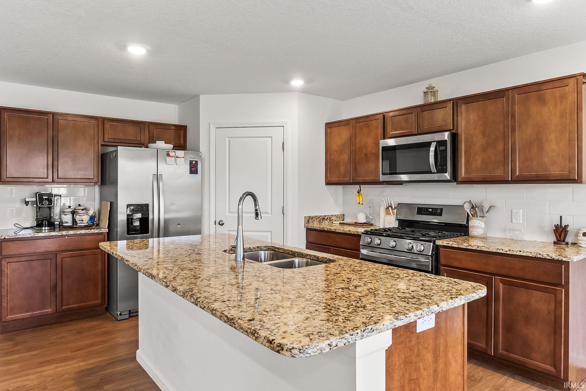 Kitchen featuring a central island with a double basin sink and a high-arc faucet, granite countertops, wood-finish cabinetry, stainless steel appliances, and wood-finish flooring