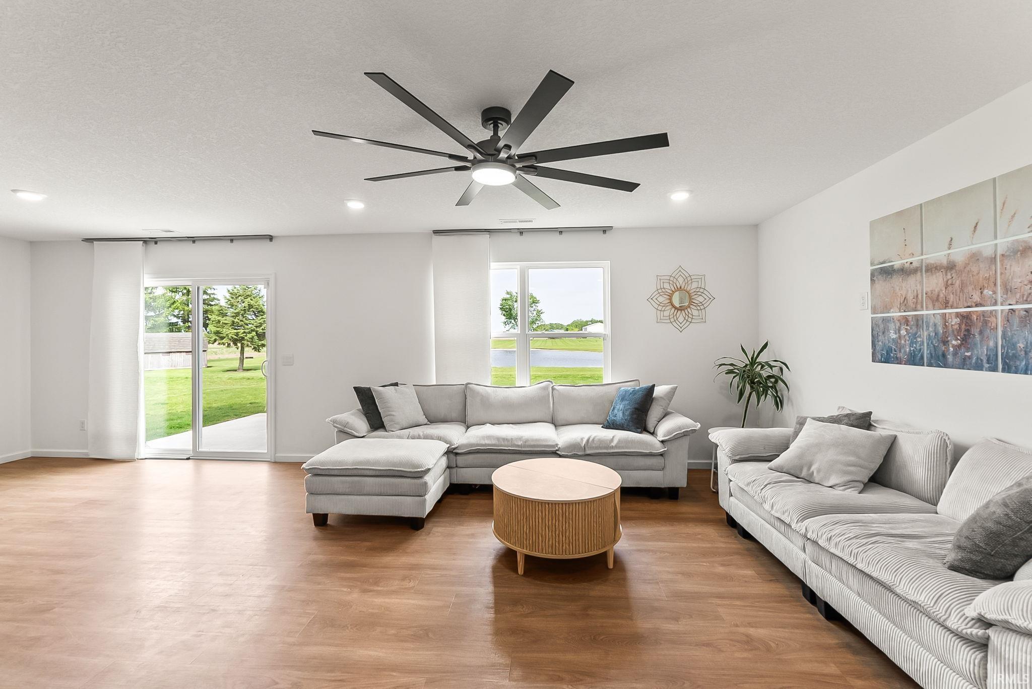 Spacious living area featuring wood-finish flooring, a modern ceiling fan with integrated lighting, and recessed ceiling lights