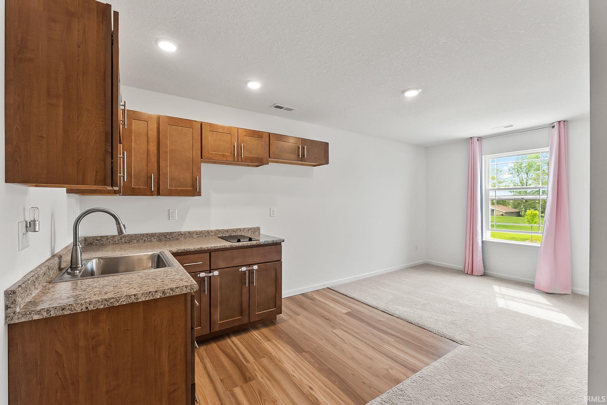 Upstairs Loft with compact kitchen area featuring wood cabinetry, stone-finish countertops, and a stainless steel sink & electric cooktop