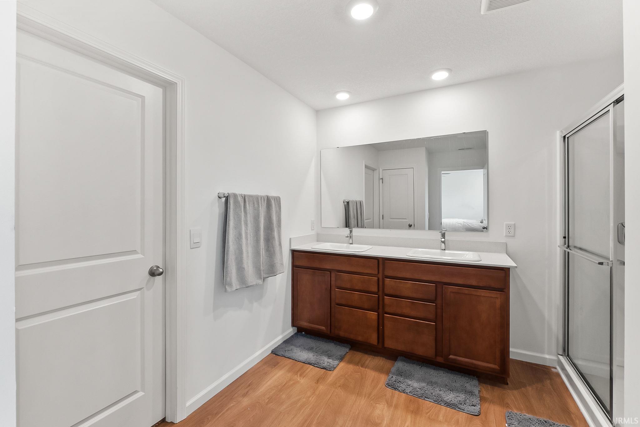 Dual sink vanity with wood-finish cabinetry and white countertop, framed by a large mirror