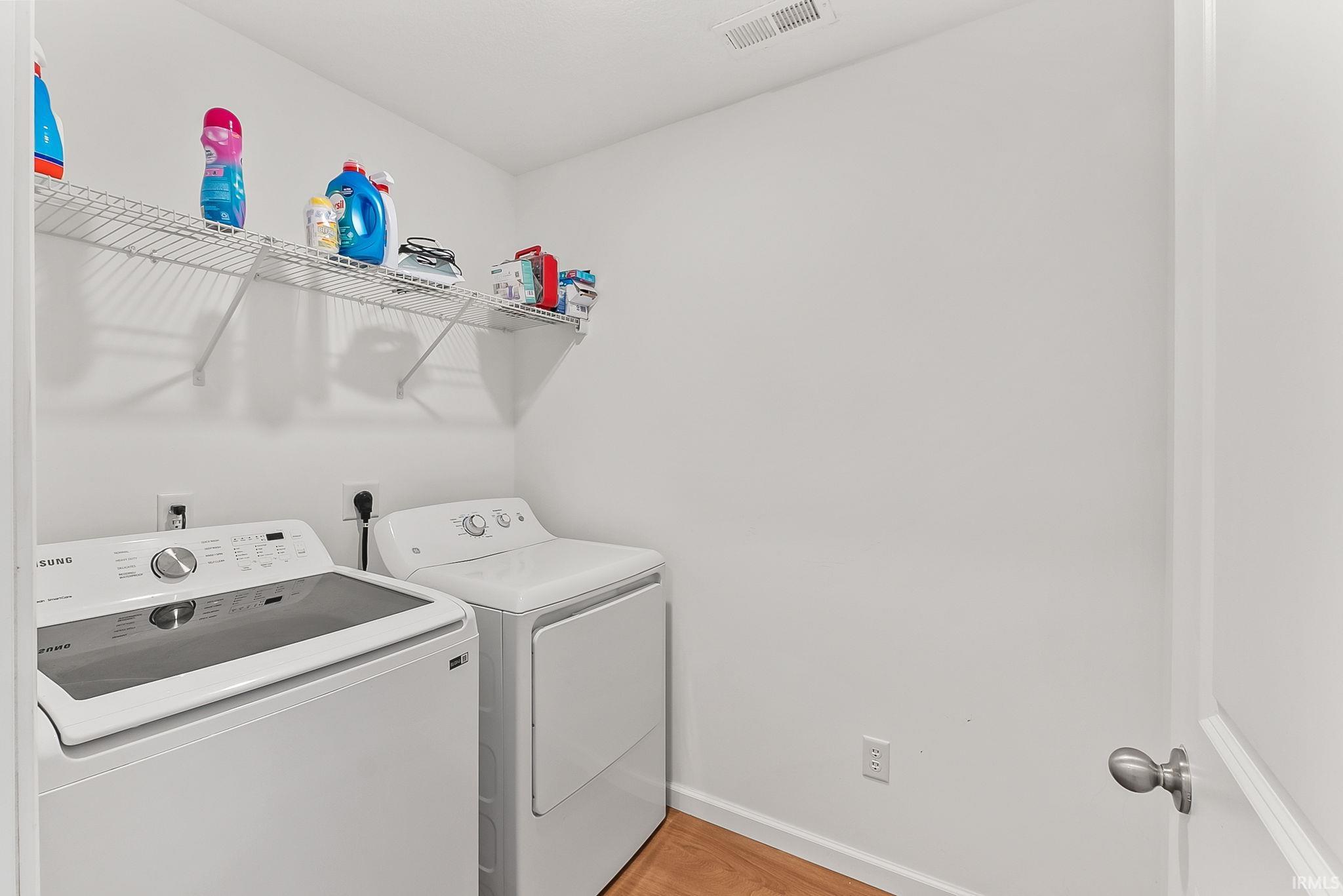 Dedicated laundry area featuring wood-finish flooring, white walls, and a convenient wire shelving unit
