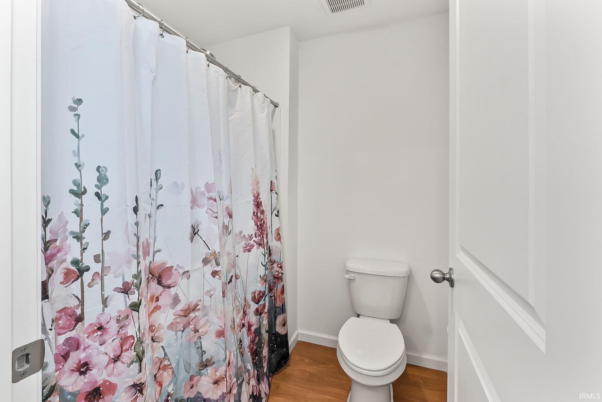 Compact bathroom featuring bright white walls, a standard toilet, and wood-finish flooring