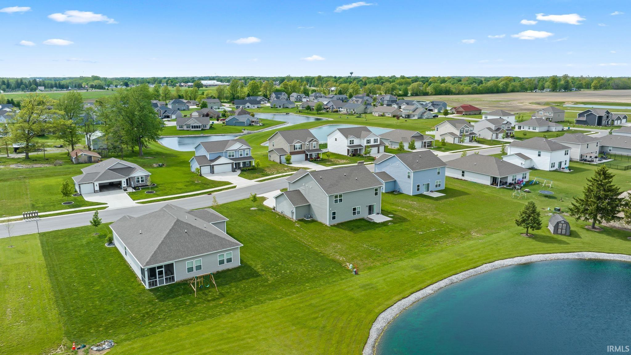 Aerial perspective showcasing a residential development with established homes, green lawns, and a tranquil pond
