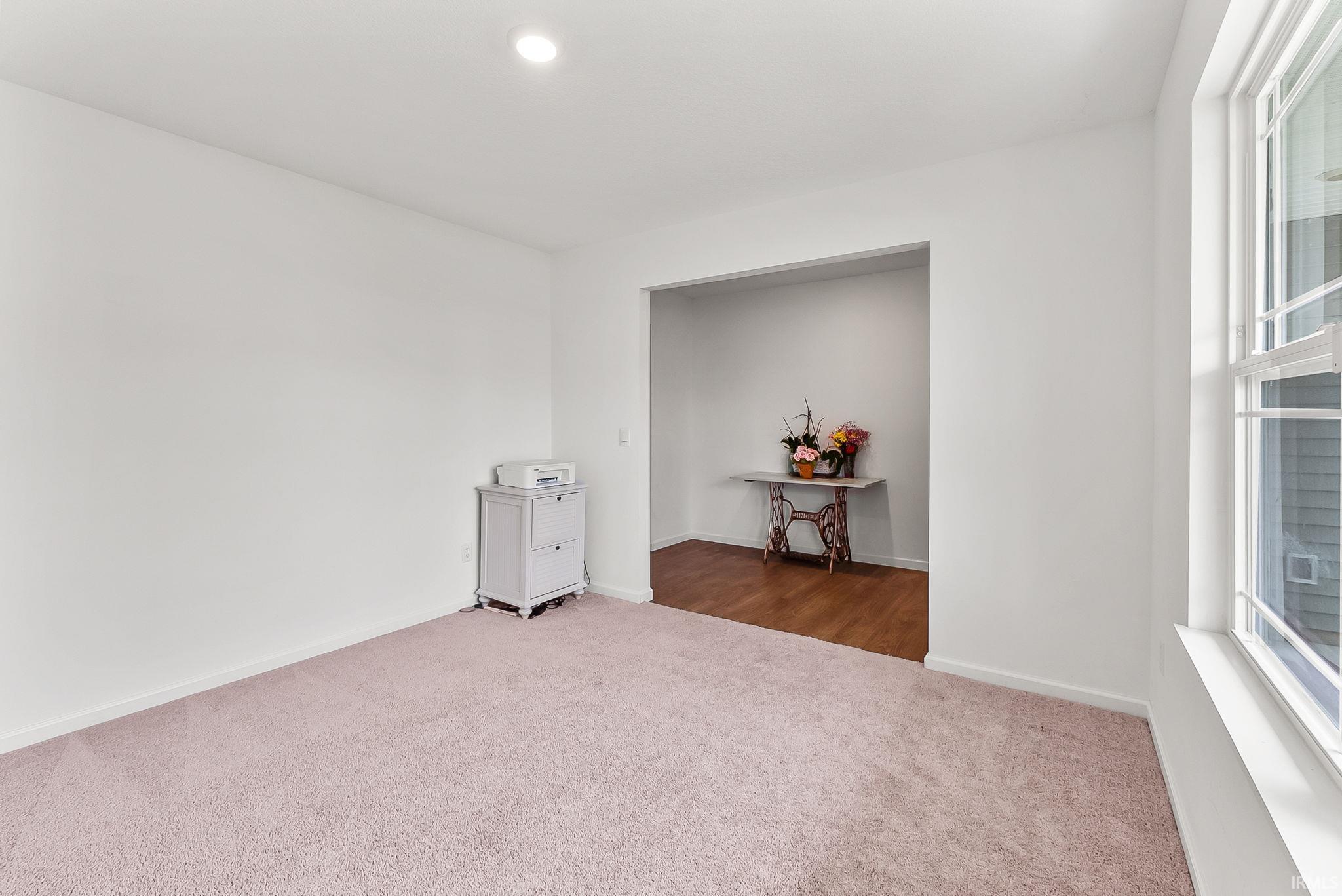 Spacious interior room featuring light-colored carpeting, white walls, and a recessed ceiling light